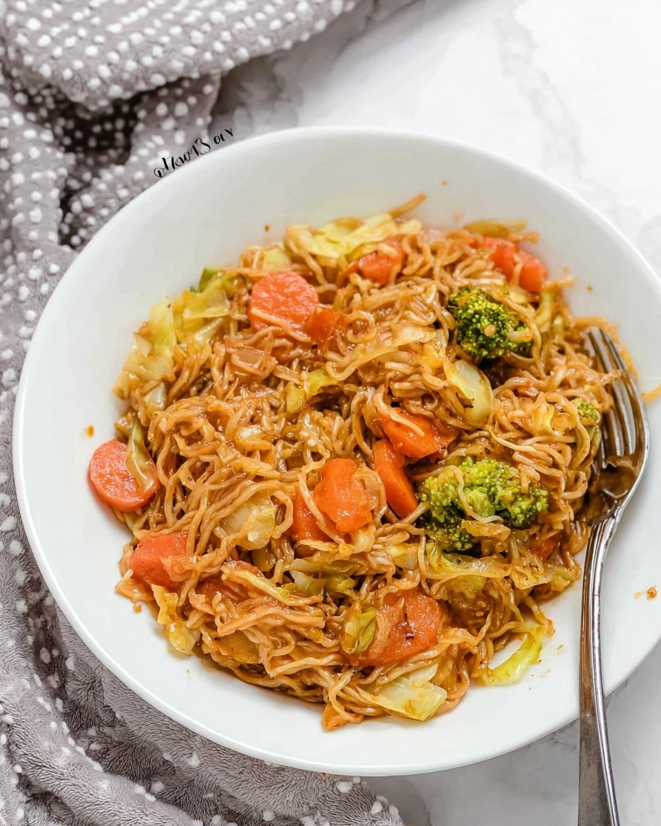 A white bowl filled with a mix of cooked noodles and vegetables. The noodles are light brown and tangled throughout the dish. Mixed in are sliced orange carrots, green broccoli pieces, and small chunks of light yellow cabbage, all coated in a savory sauce giving them a slight shine. A fork rests on the edge of the bowl, with its handle extending outward. The bowl sits on a white marbled surface with a soft gray cloth with white dots nearby. The overall look is warm and inviting. Photo taken with an iphone --ar 4:5 --v 7