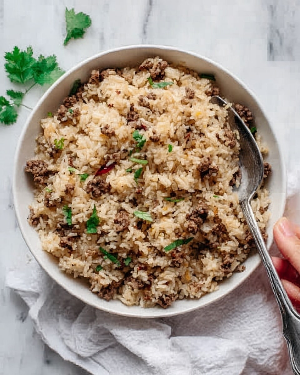 The image shows a white bowl filled with cooked rice mixed with small, crumbly pieces of brownish meat. The rice and meat are evenly spread in the bowl, with a few green herb leaves scattered on top for color. A metal fork is placed inside the bowl on the right side, resting on the rice mixture. The bowl sits on a white marbled surface with a white cloth and a woman's hand holding a fork visible in the background. Photo taken with an iphone --ar 4:5 --v 7