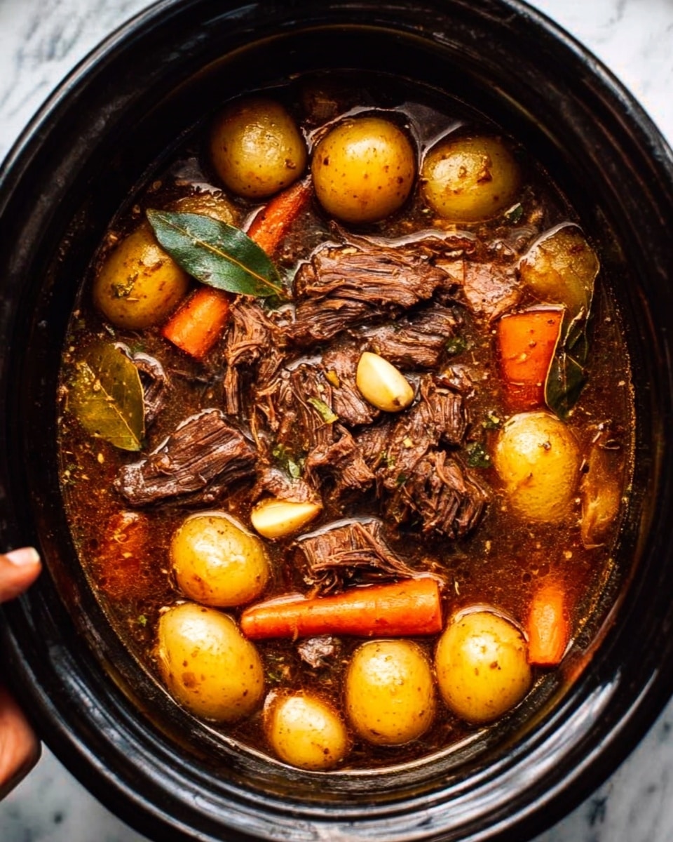 The image shows a dark pot filled with slow-cooked beef chunks and smaller shredded pieces in the center, surrounded by small golden potatoes and bright orange baby carrots. Bay leaves and a few garlic cloves float in a rich brown broth, creating a hearty stew look. The beef appears tender and juicy, and the vegetables are soft but firm. The pot sits on a white marbled surface, and a woman's hand is just visible holding the edge of the pot. photo taken with an iphone --ar 4:5 --v 7