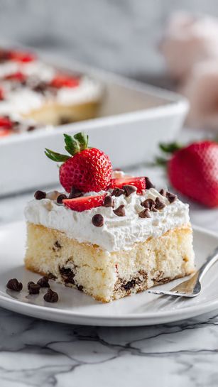 The image shows two square slices of strawberry-filled pie on a white plate, each slice with a golden-brown, slightly shiny crust that looks crisp and flaky on top. The top crust is lightly dusted with powdered sugar, and red strawberry pieces peek through the small gaps of the crust. Around the plate, there are fresh whole strawberries with green leaves and a few small dark chocolate chips scattered on a white marbled surface. In the background, a rectangular metal baking pan with more pie slices is partially visible. The photo is taken with a woman's hand holding the plate slightly from the bottom left corner. Photo taken with an iphone --ar 4:5 --v 7