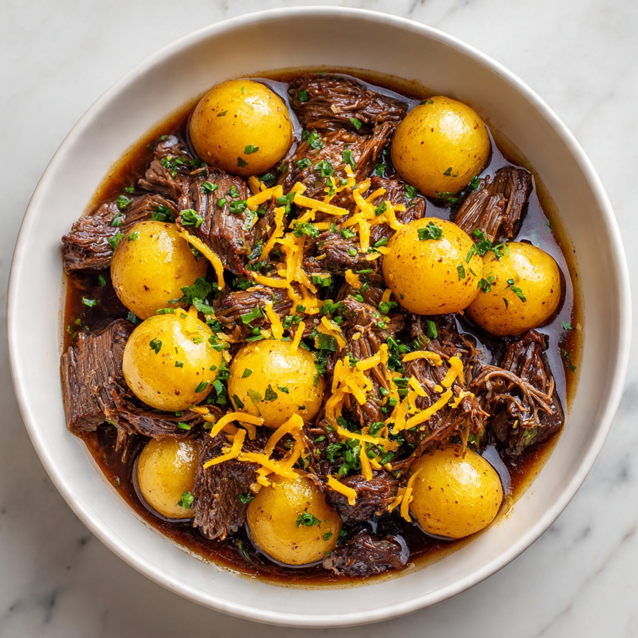 The image shows a white bowl filled with tender pieces of cooked beef mixed with small boiled yellow potatoes. The beef is dark brown, juicy, and slightly shiny, while the potatoes have smooth, yellowish skins. The dish is topped with a sprinkle of shredded orange cheese and small bits of green herbs, scattered evenly over the top. The ingredients are placed close together, creating a hearty, rich look against the white marbled background. Photo taken with an iphone --ar 4:5 --v 7