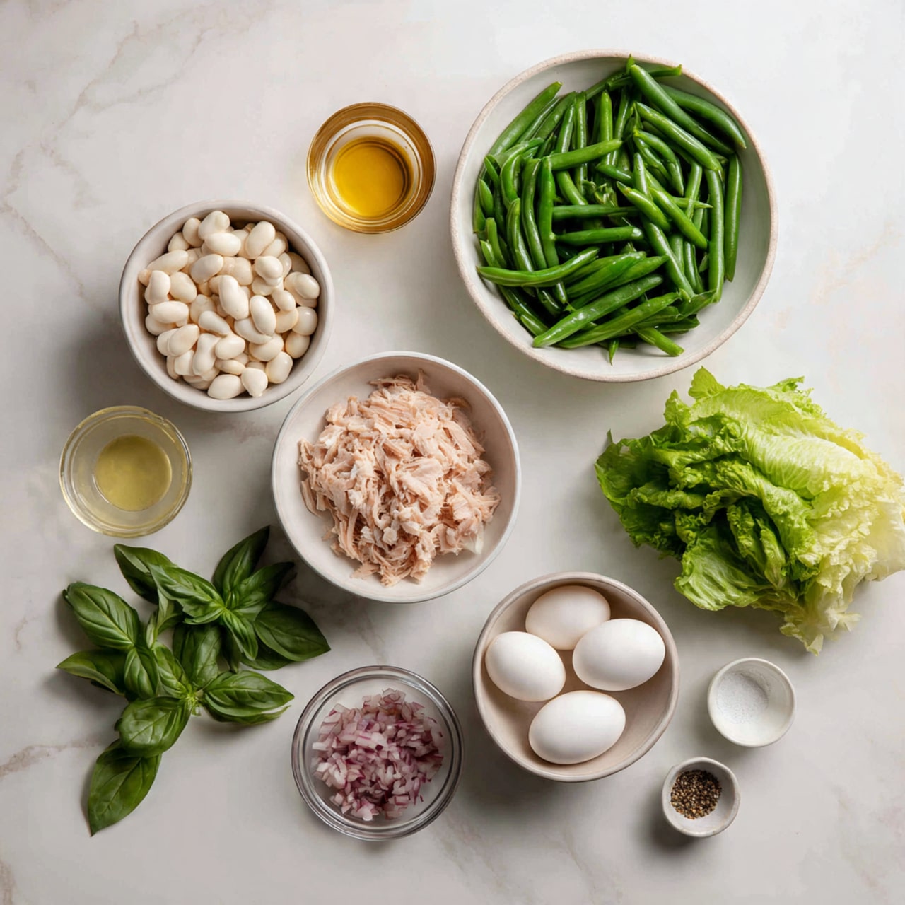 The image shows ingredients for a fresh salad laid out on a white marbled surface. There are eight containers arranged neatly: a large white bowl filled with bright green trimmed green beans at the top right, a smaller white bowl with light pink shredded tuna below it, and to its left a small round white container with white beans. Below those is a white bowl of crisp leafy green lettuce. To the right of the lettuce is a bunch of fresh basil leaves with deep green color. In front of the basil is a small clear glass bowl with finely chopped red shallots. Above the green beans are three small bowls: one with three white peeled boiled eggs, another with golden olive oil, and a smaller one with white salt and black pepper. A small glass of light amber liquid is also present near the top center. photo taken with an iphone --ar 4:5 --v 7