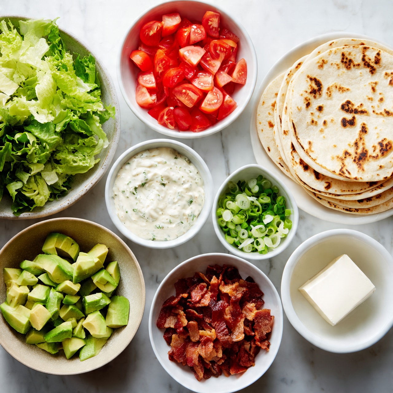 The image shows eight white bowls and plates arranged on a white marbled surface. Starting from the top right, there is a white bowl filled with a stack of plain tortillas showing light brown grill marks. To its left, a white plate holds evenly diced green avocado and bright red chopped tomatoes side by side. Above the avocado and tomato plate, there is a bowl full of mixed green leafy lettuce with various textures. Below the tomato and avocado plate, there is a small bowl with creamy white sauce. Next to it, more to the bottom left, is a small bowl filled with sliced green onions. To the right of the green onions, there is a bowl with a creamy, herb-speckled dressing. Moving right from the sauce in the center bottom, a bowl contains chopped, crispy bacon pieces in shades of reddish-brown. Lastly, to the right of the bacon bowl, a small bowl holds a thick white block of cheese or cream. The overall look is fresh with vibrant green, red, creamy white, and warm brown colors. Photo taken with an iphone --ar 4:5 --v 7