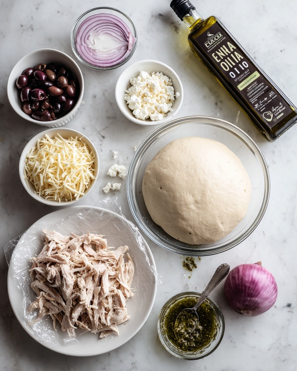 The image shows several bowls and plates of ingredients on a white marbled surface. At the center right is a large glass bowl with smooth, round, pale dough covered with plastic wrap. Below it is a white plate holding shredded light pink cooked chicken. Above the chicken, a white bowl is filled with shredded pale yellow cheese. To the right, a small white bowl holds dark purple black olives. Next to it is another small white bowl with crumbled white cheese. Above the dough, there is a half red onion with visible rings. Near the onion, a clear container holds green pesto sauce with a silver spoon inside. On the top right corner, a dark green bottle labeled