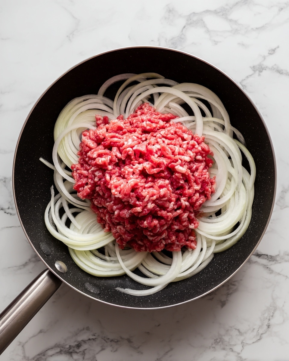 The image shows a black skillet with raw thinly sliced onions placed in a ring around the edge, creating a white and pale yellow layer. In the center of the skillet, there is a pile of raw ground meat, which is red with some lighter pink and white streaks of fat mixed in. The skillet is sitting on a white marbled surface. The photo taken with an iphone --ar 4:5 --v 7