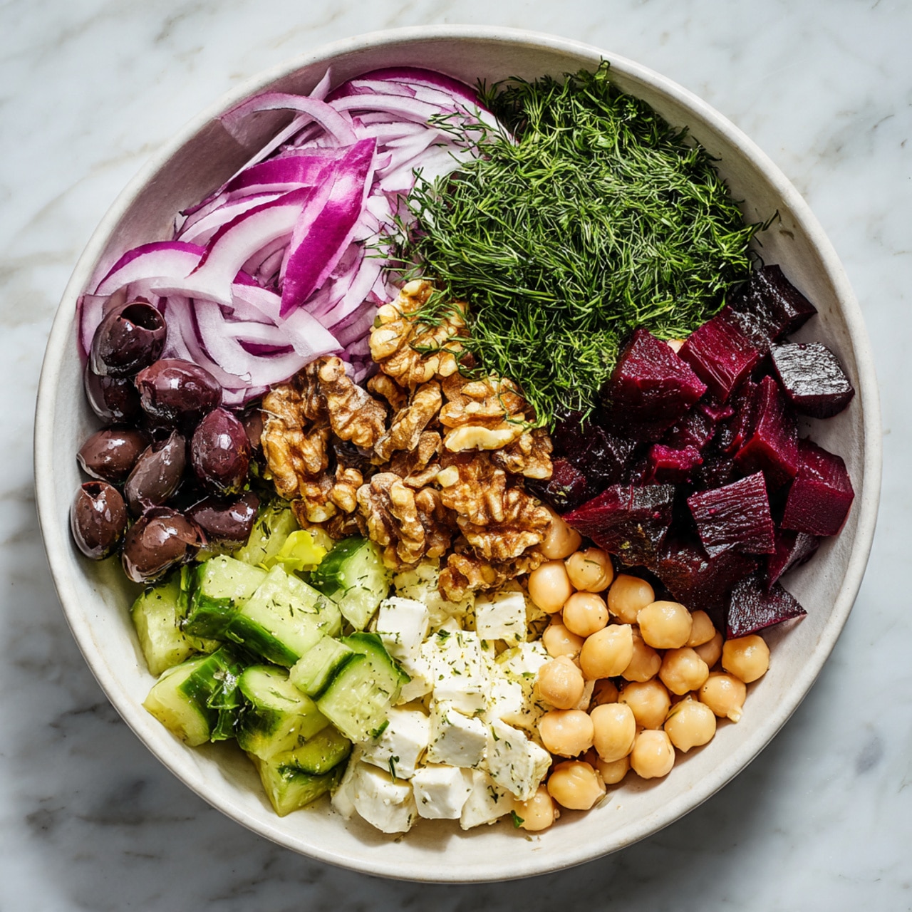 In a white bowl on a white marbled surface, there are seven visible layers arranged side by side. Starting from the top left, there are thin purple and white slices of red onion with a light watery texture, next is a small bunch of finely chopped green dill, followed by a pile of roughly chopped brown walnuts. On the top right, there are dark red, cubed beet pieces with a slightly shiny surface. Below the beets, there are smooth white cubes of cheese. To the bottom left of the cheese, there are chopped light green cucumber pieces with darker green skin, and to the left of the cucumber, there are dark purple black olives with a shiny appearance. In the center of the bowl, there is a pile of round, beige chickpeas with a smooth look. Photo taken with an iphone --ar 4:5 --v 7
