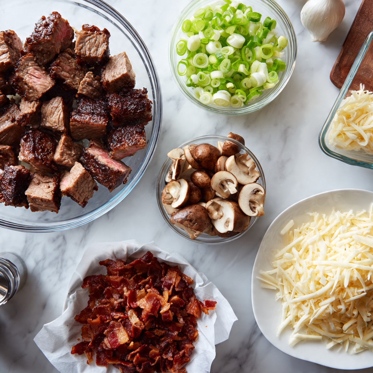 Beef & Smoked Cheddar Potato Soup Recipe 4 The image shows several containers and a plate with different food ingredients arranged neatly on a white marbled surface. A large clear glass bowl is filled with grilled meat pieces, some sliced pink inside with a dark brown crust, and smaller browned pieces beside them. To the right, a white plate holds a pile of finely shredded pale yellow cheese. Above the plate, a small clear bowl contains sliced green onions, showing a mix of light green and white circles. Next to that, a small plastic container holds sautéed brown mushrooms with a slightly shiny surface. In the lower part of the image, a medium clear glass bowl lined with white paper holds crispy reddish-brown bacon bits. The setting includes a few kitchen items in the background, but the focus is on the food elements. photo taken with an iphone --ar 4:5 --v 7