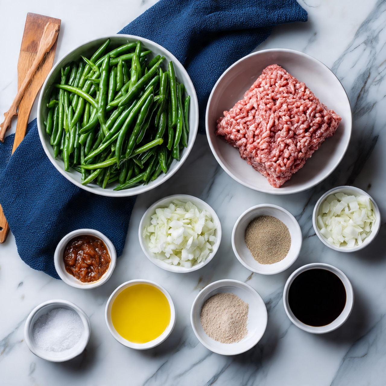 The image shows a collection of ingredients arranged neatly on a white marbled surface. There is a large white bowl filled with frozen green beans, placed next to another large white bowl holding a square block of raw ground meat that has a pinkish-red color and a textured surface from the grinding. Surrounding these are smaller white bowls containing chopped white onions, minced garlic, and a reddish-brown paste. Below these bowls, there are several small white dishes with different liquids and powders, including a bright yellow liquid, a dark soy-like sauce, white granulated salt, a light beige powder, and a brown powder. A dark blue cloth and a wooden spatula rest in the upper area near the bowls. photo taken with an iphone --ar 4:5 --v 7