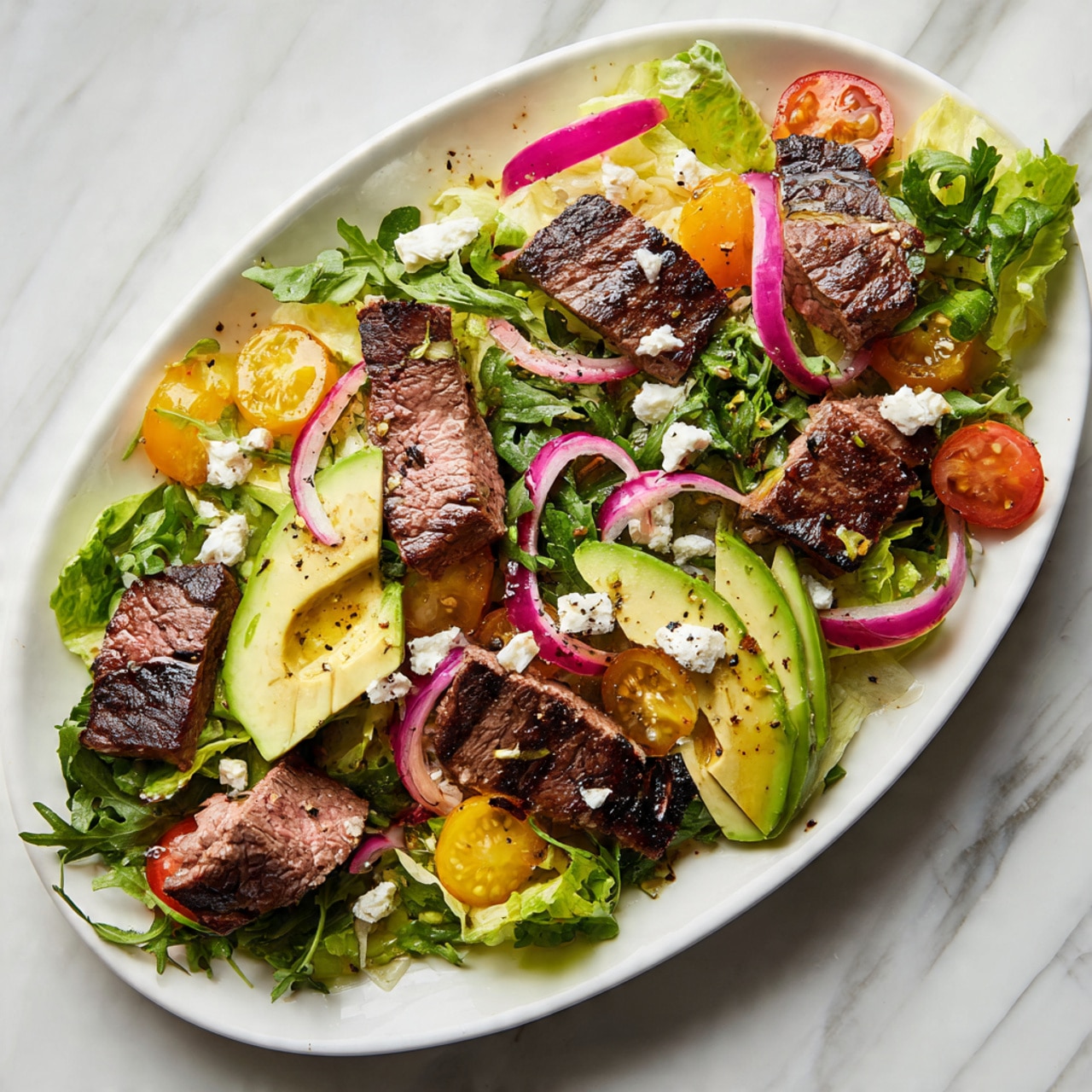 This dish is arranged on a white oval plate set on a white marbled surface. The base layer is a mix of green leafy arugula and light yellow lettuce, spread evenly across the plate. On top, there are several slices of grilled steak, each showing a seared dark brown edge with a pink center, positioned in separate small clusters around the plate. There are also thin slices of avocado with a smooth light green color and a drizzle of oil on them, placed near the steak groups. Bright red and golden orange cherry tomato halves are scattered around the greens, adding vibrant color. Thin rings of pale purple pickled onions are placed evenly across the salad. Small crumbles of white feta cheese are sprinkled all over the dish. The entire salad looks fresh with a light sprinkle of black pepper. Photo taken with an iphone --ar 4:5 --v 7