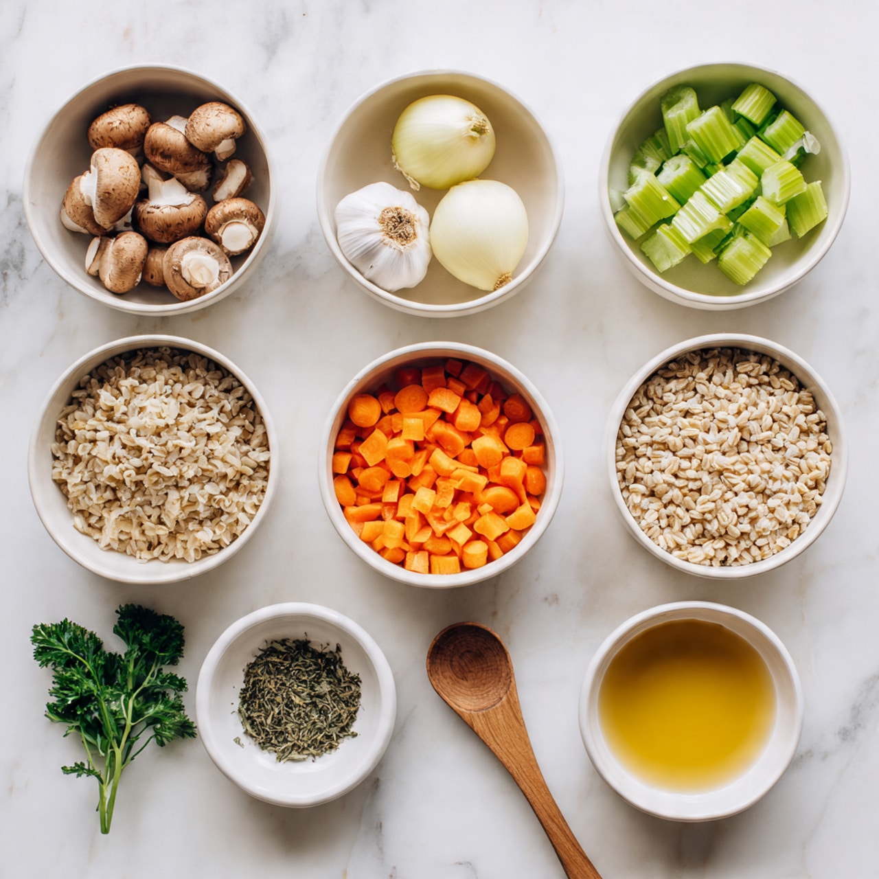 The image shows a white marbled surface with eight white bowls arranged neatly. In the top row, from left to right, there is a bowl filled with brown mushrooms, a bowl with light yellow onion, and a whole garlic bulb. The middle row has a bowl of green celery pieces on the left, a bowl of chopped orange carrots in the center, and a bowl of beige barley on the right. At the bottom, a bowl with mixed green parsley leaves is on the left, a small bowl with dried green herbs and a wooden spoon in the center, and a bowl with golden-yellow liquid, possibly broth or oil, on the right. A woman's hand is partially visible in the lower corner, adjusting the bowl with herbs. photo taken with an iphone --ar 4:5 --v 7