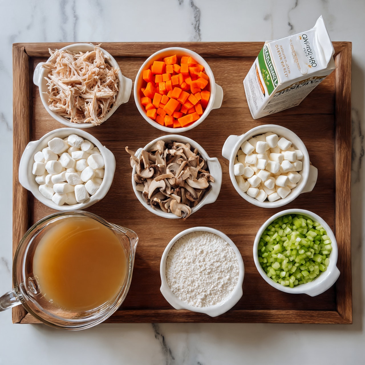 The image shows a wooden tray with nine small white bowls arranged neatly, each filled with different ingredients: sliced orange carrots, shredded cooked white chicken, sliced brown mushrooms, chopped green celery, cooked wild rice, and small white marshmallows. There is also a bowl with white flour and a clear bowl with a clear liquid. In front of the tray, there is a glass measuring cup filled with light brown broth and a carton of organic half-and-half cream. The background surface is a white marbled texture. photo taken with an iphone --ar 4:5 --v 7