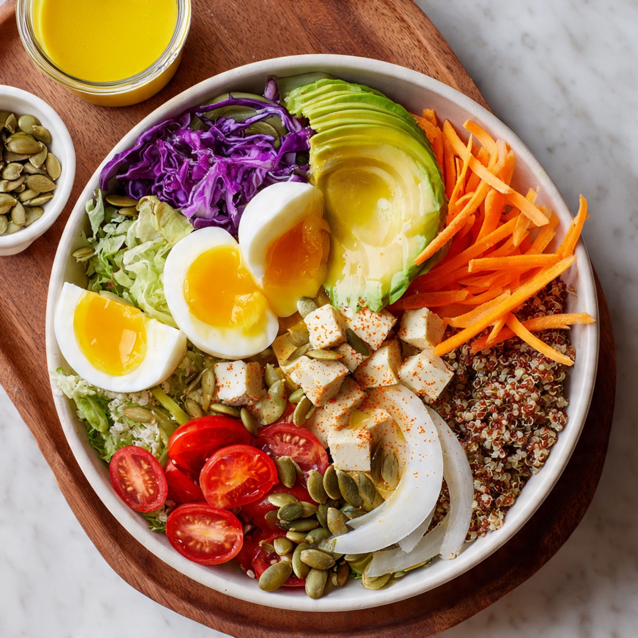 A white bowl filled with a colorful salad is shown on a white marbled surface. The bowl has two halved boiled eggs with bright yellow yolks placed on opposite sides near the edge. Next to the eggs, there are fresh, light green broad beans in one part, bright red halved cherry tomatoes with a shiny texture, and thin shredded orange carrot strips stacked next to the tomatoes. Near the center, there is a layer of fluffy light brown quinoa and chopped light beige tofu cubes beside it. Above the tofu, some purple shredded cabbage adds vibrant color. Thin white onion slices are placed on top in the middle. A sliced avocado fan with a smooth, green texture sits near the center, sprinkled with a light spice powder. A generous pile of green pumpkin seeds is placed near the center over the quinoa and cabbage. The whole dish rests on a wooden tray with a small glass bowl of yellow dressing and another bowl holding extra pumpkin seeds visible in the background photo taken with an iphone --ar 4:5 --v 7