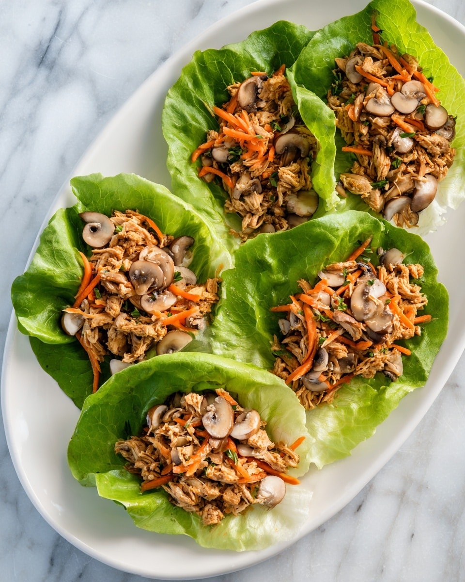 A white oval plate on a white marbled surface holds four lettuce wraps, each made with bright green lettuce leaves as the base. On top of the lettuce, there is a mix of light brown shredded chicken-like pieces, fine orange shredded carrots, and small white sliced mushrooms. The textures contrast with the fresh crisp lettuce, soft mushrooms, and chewy chicken-like mix, arranged neatly in individual wraps. The colors are fresh and vibrant with green, orange, white, and light brown tones. photo taken with an iphone --ar 4:5 --v 7