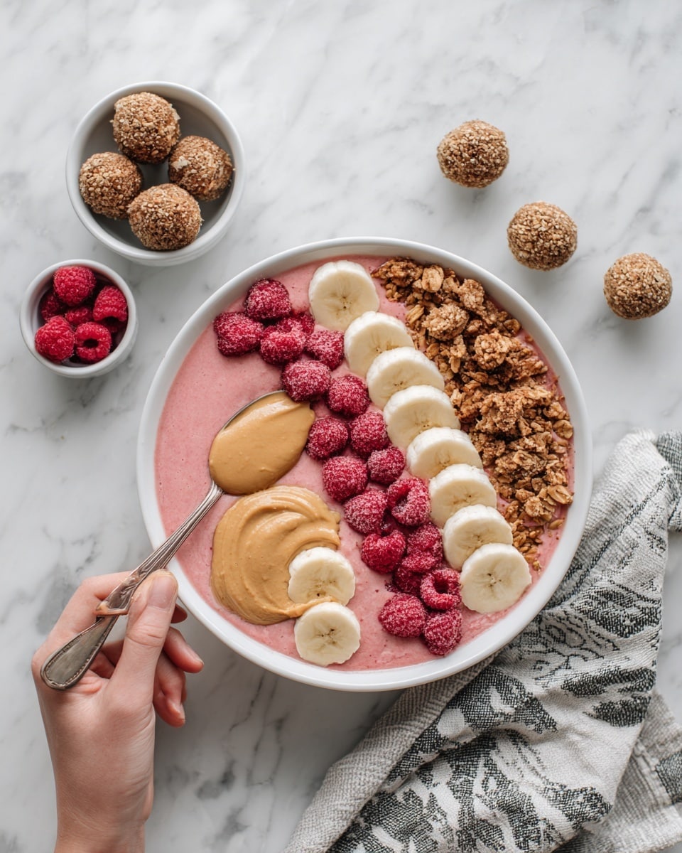 The image shows a white bowl filled with layers of food placed on a white marbled surface. The bottom layer is a smooth pink smoothie. On top, there are six round slices of light yellow banana arranged along one side. Next to the bananas, there is a thick line of reddish-pink crushed raspberries. In the center, towards the top, there is a pile of brown granola clusters. Beside the granola, a dollop of creamy light brown peanut butter is placed. Around the bowl, there are small white bowls holding banana slices, raspberries, and six round brown energy balls. A woman's hand holds a spoon inside the bowl. A cloth with a gray and white pattern lies near the bowl. The overall scene is bright and clean. photo taken with an iphone --ar 4:5 --v 7