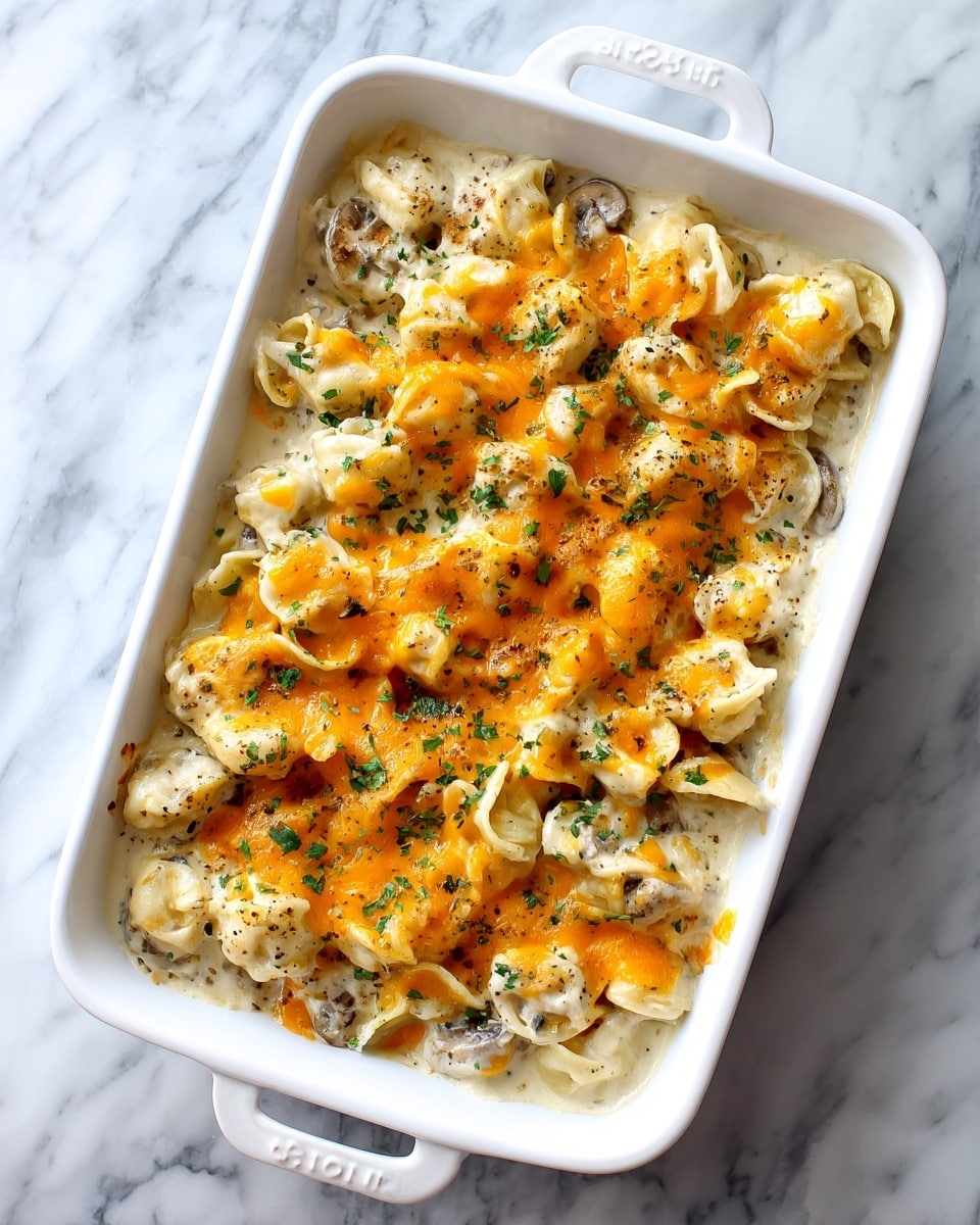 A white baking dish filled with creamy pasta topped with melted orange cheese and small green herbs scattered on top; the pasta appears to be curly and well coated with a white sauce mixed with small mushroom pieces visible underneath the cheese layer, all set on a white marbled surface photo taken with an iphone --ar 4:5 --v 7