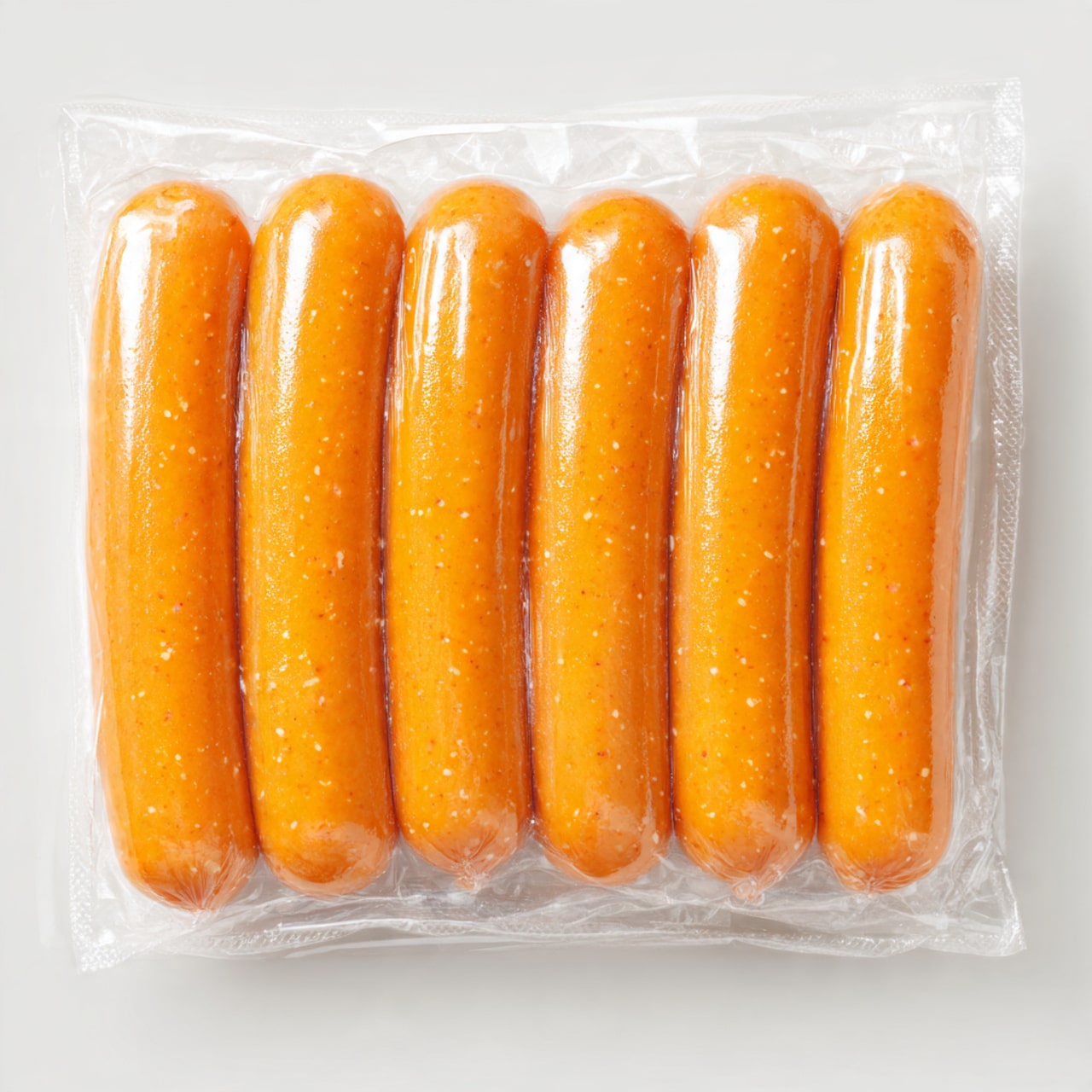 The image shows a pack of six smooth, orange sausages neatly arranged in two rows of three, sealed tightly in clear plastic. The sausages have a consistent, shiny texture with small specks visible within the meat. The background is a white marbled surface, making the sausages the clear focal point. Photo taken with an iphone --1:1