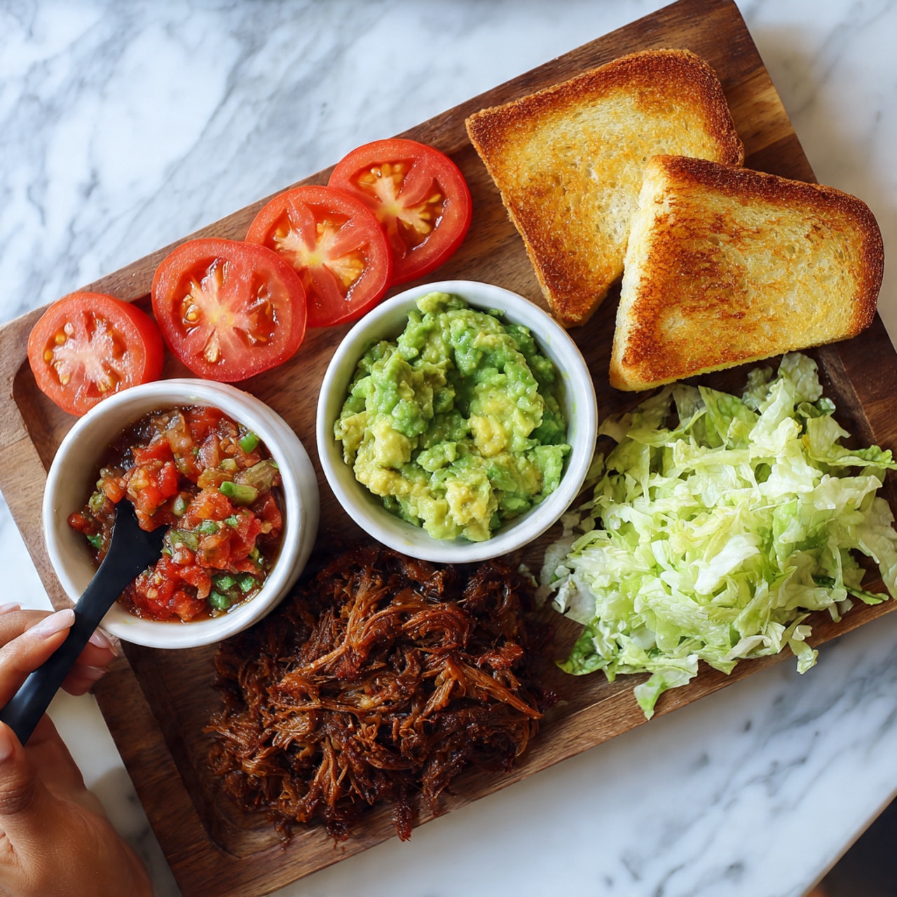 The image shows a wooden board with several food items arranged neatly. On the left side, there is a small white bowl filled with chunky red salsa and another small white bowl with green guacamole, with a woman's hand holding a black spoon resting in it. Next to these bowls are slices of juicy red tomatoes layered one on top of another. To the right, there are three toasted slices of bread stacked slightly overlapping. Below the tomatoes, there is a pile of shredded cooked meat with a rich brown color. On the bottom right corner of the board, shredded pale green lettuce is neatly placed. The whole scene is set on a white marbled surface. Photo taken with an iphone --ar 4:5 --v 7