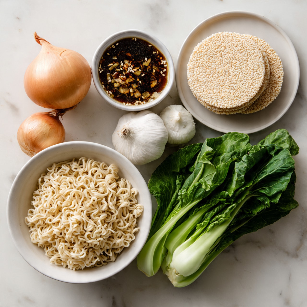 A white bowl containing a light brown onion with a slightly rough layer, two white garlic bulbs with smooth, papery skin, and a bunch of green leafy vegetables with thick stems placed on a white marbled surface. Beside the bowl, there is a block of textured pale beige uncooked ramen noodles, and above the bowl is a small white bowl filled with a dark brown liquid topped with sesame seeds and pieces of minced ingredients. To the top right, there is a stack of roundish, light mauve rice cakes on a white plate. Photo taken with an iphone --ar 4:5 --v 7