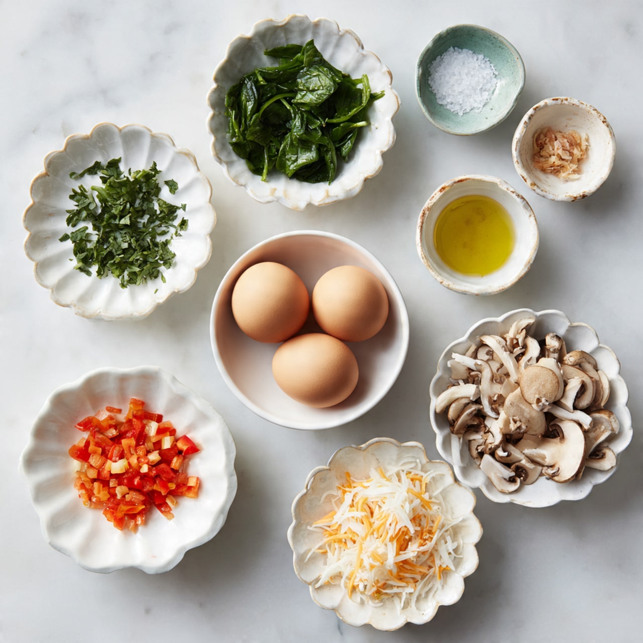 The image shows nine small white dishes with different ingredients arranged on a white marbled surface. In the center is a round white bowl holding three brown eggs. Around it, starting from the top left, is a scallop-edged bowl with green spinach leaves, a small bowl with white salt crystals, a white bowl filled with yellow oil, another scallop-edged bowl containing small chopped red bell pepper pieces, a small white bowl with chopped green herbs, a scallop-edged bowl with finely diced white onions, a white plate with shredded orange cheese, and finally a scallop-edged bowl with chopped brown mushrooms. The overall arrangement is neat and balanced with a soft natural light. Photo taken with an iphone --ar 4:5 --v 7