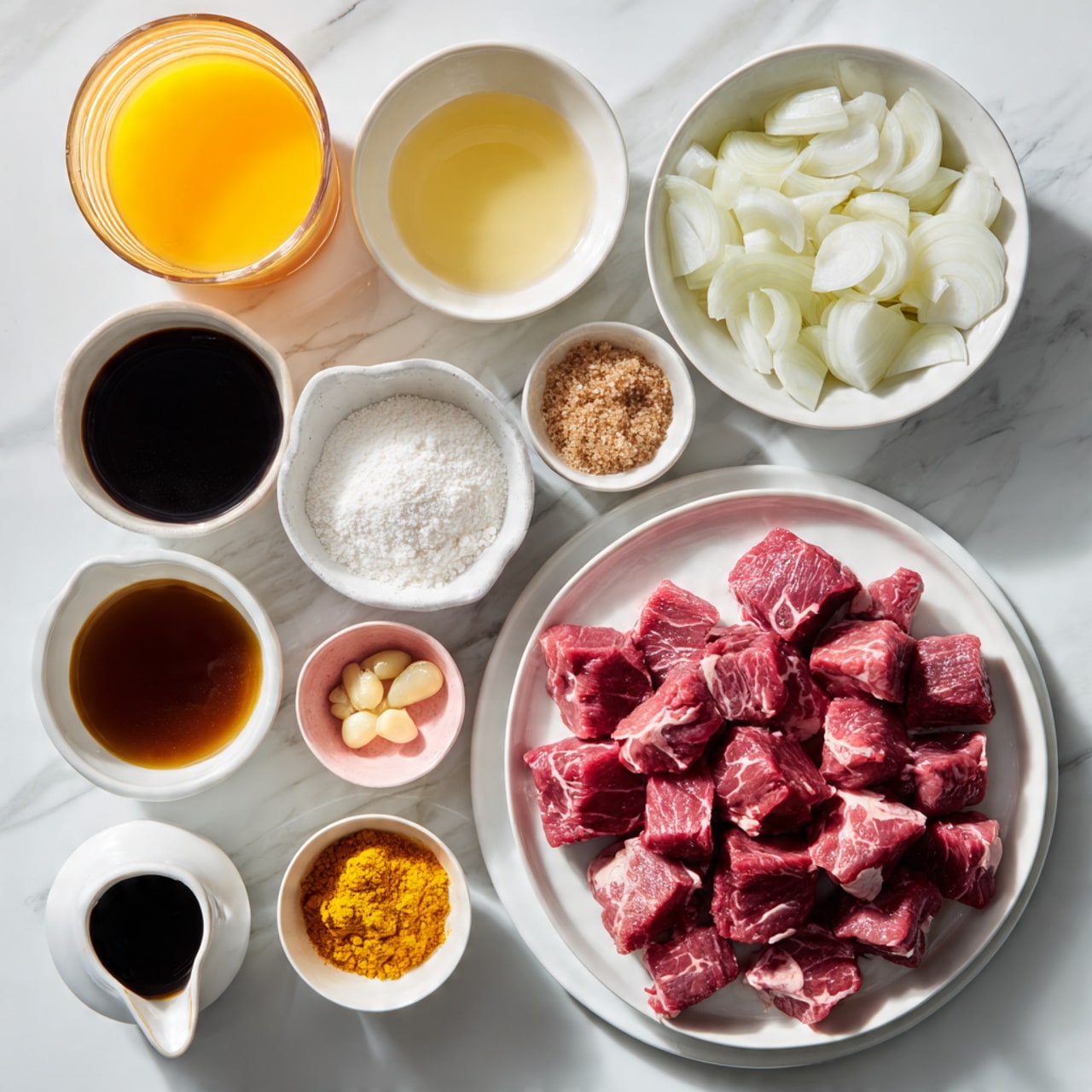 The image shows an arrangement of cooking ingredients on a white marbled surface. On the right side, there is a white plate full of raw red meat cubes with some white fat parts visible. Above it, there is a small white bowl filled with quartered white onions and next to it a smaller white bowl with brown sugar. Above the onions and slightly to the left, there is a white bowl with a light yellow liquid. Below it, a small white bowl contains sliced white garlic cloves. Left of the garlic, there is a small pink bowl filled with grated ginger and above it a small white bowl of flour. Below the ginger bowl, there is a small white bowl with a bright yellow turmeric powder. To the left bottom corner, a white jug contains a dark brown liquid and next to it a small white bowl of light brown liquid. Next to that, a small white jug holds black soy sauce with a shiny texture. At the top left, a clear glass jug contains orange juice. The setup is neat and bright, with all bowls and plates in white except the pink bowl for ginger. Photo taken with an iphone --ar 4:5 --v 7