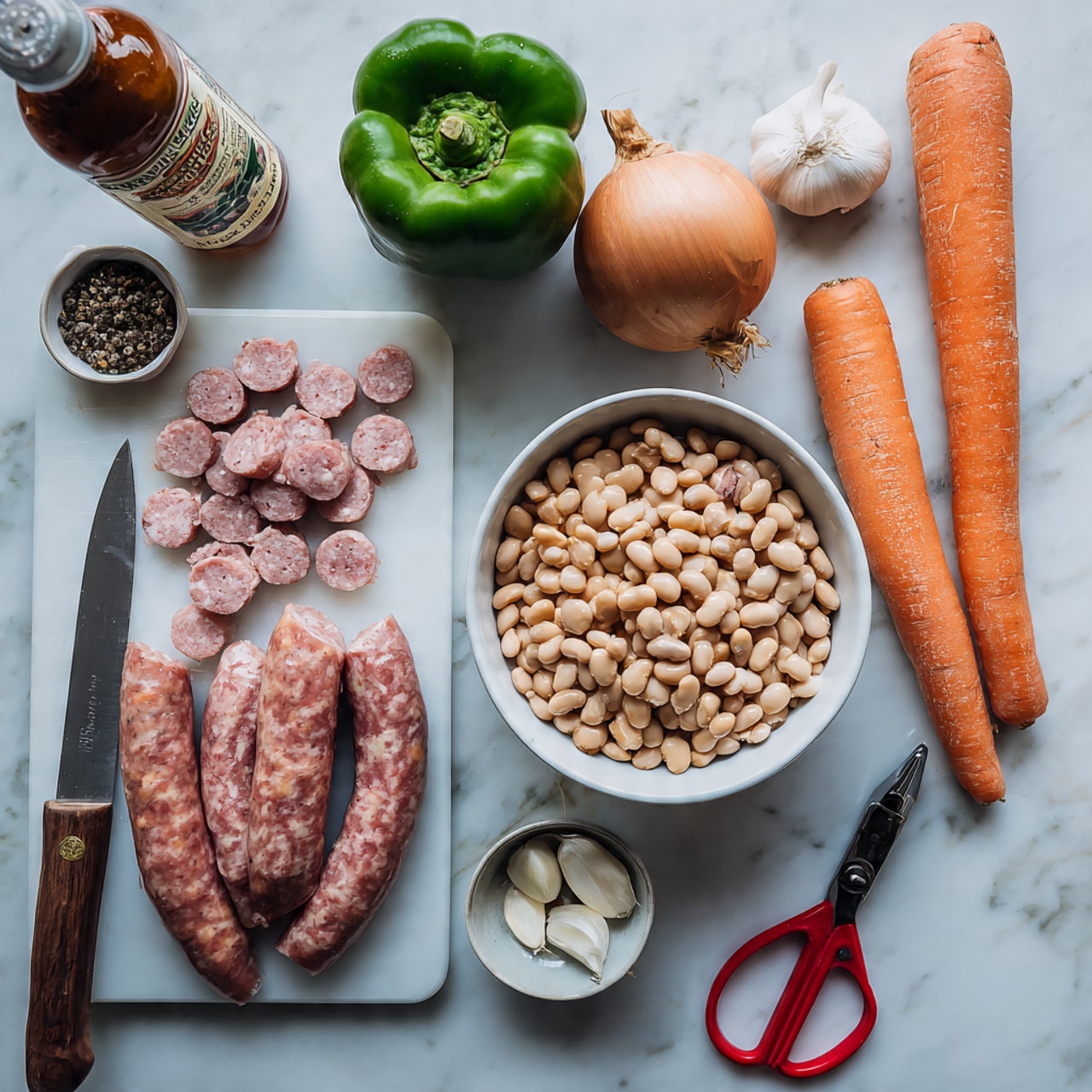 The image shows a clear white bowl filled with two types of beans, pale beige and light brown, placed on the right side of the frame against a white marbled surface. To the left, there is a white cutting board with chopped and whole sausage links arranged in layers – sliced round sausage pieces with a pinkish interior and brownish outer skin, and two whole curved sausages at the bottom. A large knife lies on the cutting board with a portion of sausage being cut. Above the cutting board, a green bell pepper, a whole onion with dry roots, and several cloves of garlic are displayed. On the far right, two long orange carrots are placed vertically. Additional items include a bottle of Worcestershire sauce at the top left, a small white bowl with black pepper, a manual garlic press, and red scissors, all laid on the white marbled surface. Photo taken with an iphone --ar 4:5 --v 7