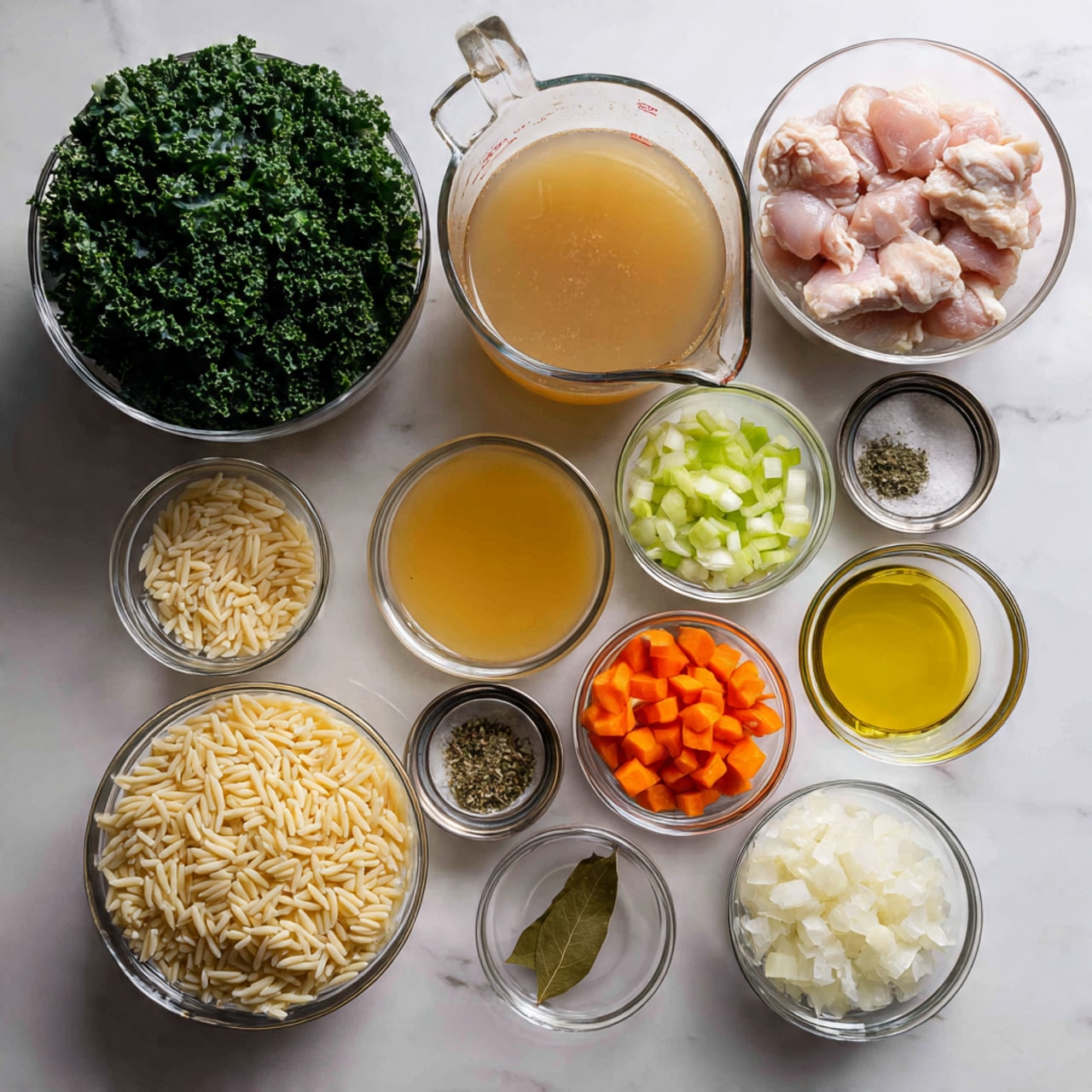 The image shows a white marbled surface with several clear glass bowls arranged neatly. The largest bowl on the left is filled with green kale leaves. Next to it, a medium bowl contains raw pink chicken pieces. Above this, there is a large clear measuring cup holding light brown broth. Below the chicken, small bowls contain diced white onions, bright orange carrots, and green celery. Around these, smaller bowls hold seasonings: yellow melted butter, a bay leaf in a silver bowl, chopped garlic, dried herbs, and salt. Near the bottom left, a bowl holds uncooked orzo pasta with a pale beige color. The lighting is bright, and the colors of the ingredients stand out clearly on the white marbled background. photo taken with an iphone --ar 4:5 --v 7