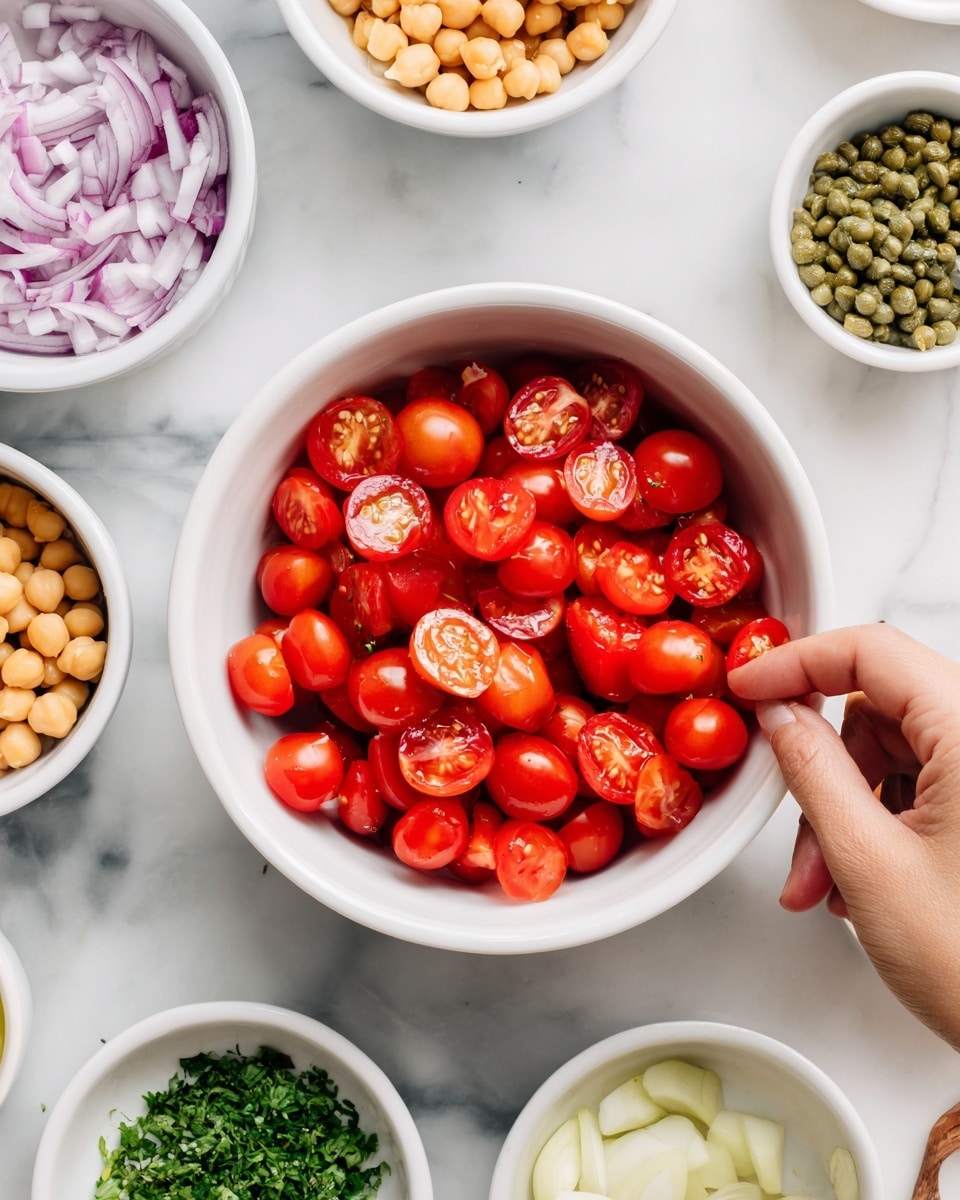 The image shows a white bowl in the center filled with bright red cherry tomatoes that are halved, showing their juicy inside and smooth skin. Around this main bowl, there are smaller white bowls placed on a white marbled surface. One bowl contains thinly sliced light purple onions, another has light golden chickpeas, a small dish with green chopped herbs, one with green capers, and another bowl with pale yellow, sliced garlic. The bowls are neatly arranged and the colors are fresh and vibrant, making a clean and fresh cooking setup. A woman's hand is gently reaching from the side toward the bowls. Photo taken with an iphone --ar 4:5 --v 7