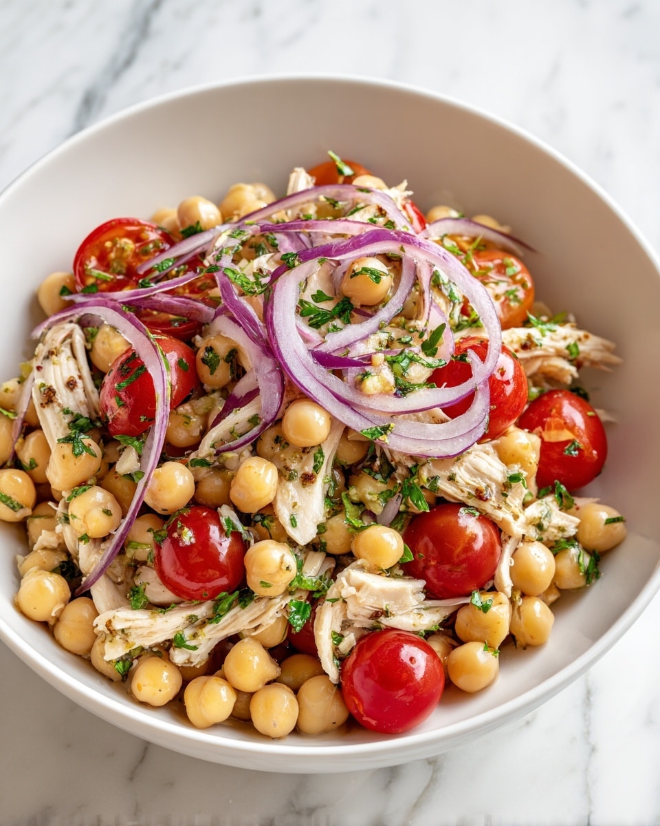 A white bowl filled with a colorful salad. The bottom layer is light beige chickpeas, scattered evenly. On top of the chickpeas are pale yellow chicken pieces, cut into strips and mixed well. Bright red cherry tomato halves are spread over the chicken, adding a fresh look. Thin slices of purple-red onion rings are placed on top, giving a crisp texture. Green herbs finely chopped are sprinkled all over the salad for extra color. The bowl is set on a white marbled surface. Photo taken with an iphone --ar 4:5 --v 7
