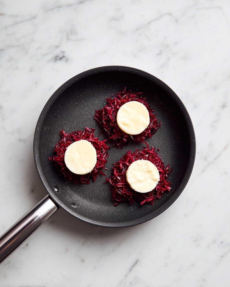 The image shows a black non-stick frying pan placed on a white marbled surface. Inside the pan, there are three small round piles of shredded red beet. Each beet pile is topped with a round slice of white cheese, creating a contrast in colors and textures. The beet looks moist and shredded finely, while the cheese slices are smooth and thick, placed in the center of each pile. The pan’s handle extends to the left, appearing clean and simple. photo taken with an iphone --ar 4:5 --v 7