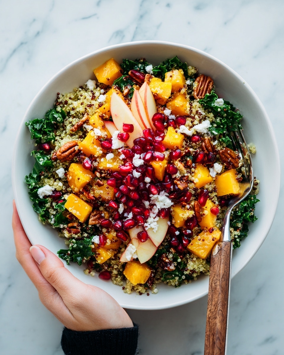 A bowl filled with a colorful salad shows three main layers: a base of small yellow quinoa grains mixed with deep green kale leaves, followed by bright orange squash cubes and thin red apple slices scattered through the bowl, and topped with clusters of red pomegranate seeds and white crumbles of cheese, all mixed with a few brown pecans for texture. The salad is placed on a white marbled surface, and a fork with a wooden handle rests inside the bowl. A woman's hand is holding the bottom left side of the bowl. Photo taken with an iphone --ar 4:5 --v 7