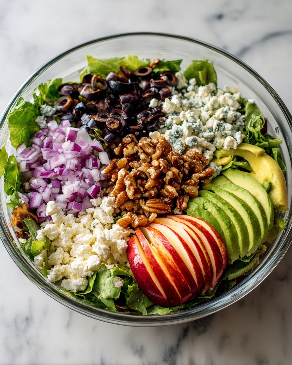 A clear glass bowl on a white marbled surface contains a colorful layered salad. At the bottom, there is a layer of fresh leafy greens. On top, from left to right, there are finely chopped black olives, crumbled white cheese, thin slices of purple-red onion, sliced green avocado, a pile of brown crunchy nuts, and in the center foreground, a sliced red apple with a visible white inside. The colors contrast well, with the dark olives, bright green avocado, and red apple pieces distinct. The photo taken with an iphone --ar 4:5 --v 7