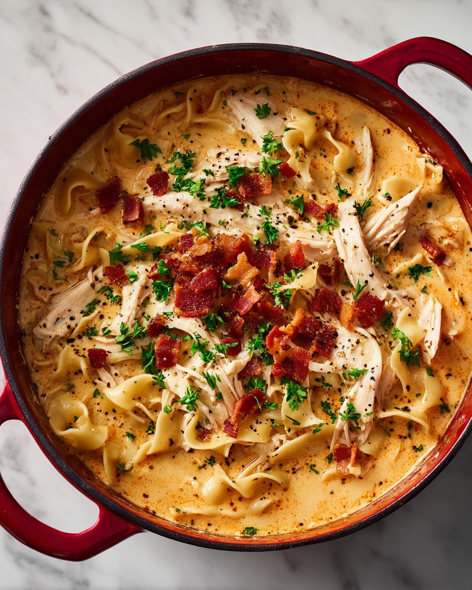 The image shows a deep red pot filled with a creamy noodle soup. The base is a thick, light orange broth with egg noodles floating throughout. On top of the noodles are shredded white chicken pieces evenly spread along with small crispy bacon bits that add a reddish-brown color. Small green parsley leaves are scattered across the surface, adding a fresh touch. The soup is sprinkled with black pepper for extra texture. The pot is sitting on a white marbled surface. photo taken with an iphone --ar 4:5 --v 7