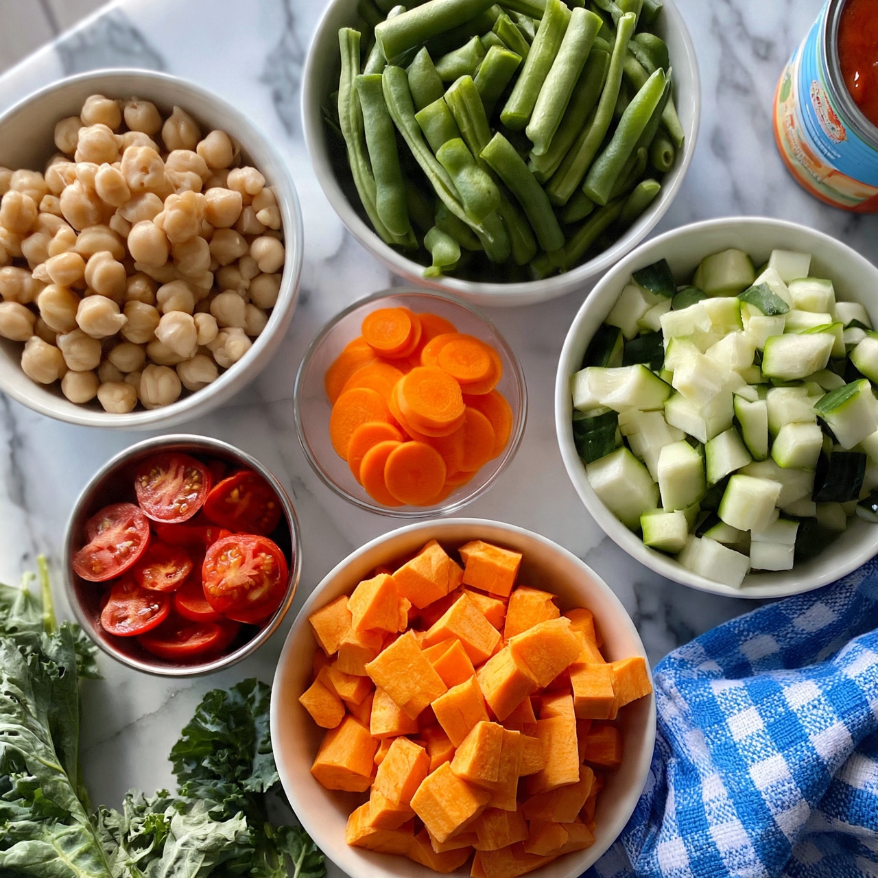 square image The image shows several white bowls and a small clear bowl on a white marbled surface, each filled with different fresh ingredients. One bowl holds a pile of chopped sweet potatoes in bright orange cubes near the bottom center. To the right, another bowl contains diced zucchini pieces in light green and white. Above it is a bowl filled with cut green beans, which are long and green. On the left side, a bowl is filled with round, beige chickpeas. A small clear bowl with round, thin slices of bright orange carrots sits between the green beans and chickpeas. Just below it is a metal cup filled with halved cherry tomatoes, showing their red skin and juicy interiors. Fresh green kale leaves are peeking from the lower left corner. A blue and white checkered cloth is spread on the bottom right edge, and a can with red sauce is partially visible on the top right corner. photo taken with an iphone --ar 4:5 --v 7