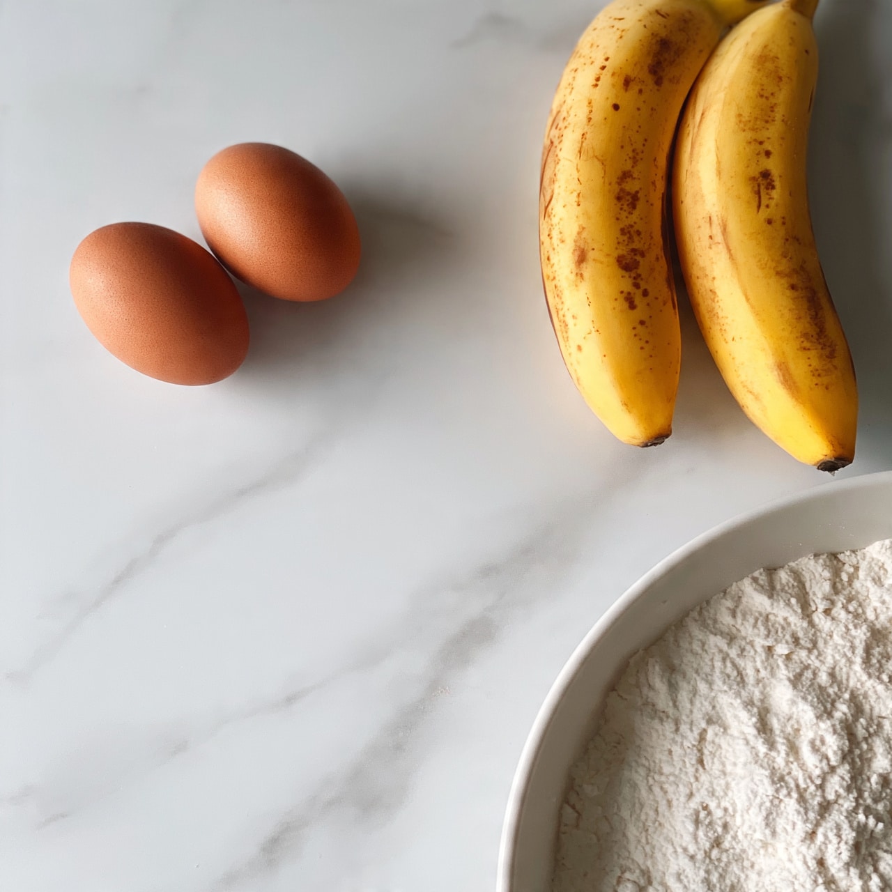 square image The image shows two whole brown eggs placed side by side on the left side of a white marbled surface. On the right side, there are two ripe yellow bananas with brown spots, laid next to each other. Below these, there is part of a white bowl filled with white flour, visible from the top edge. The arrangement is simple and clean, with the ingredients spaced out on the white marbled surface. photo taken with an iphone --ar 4:5 --v 7