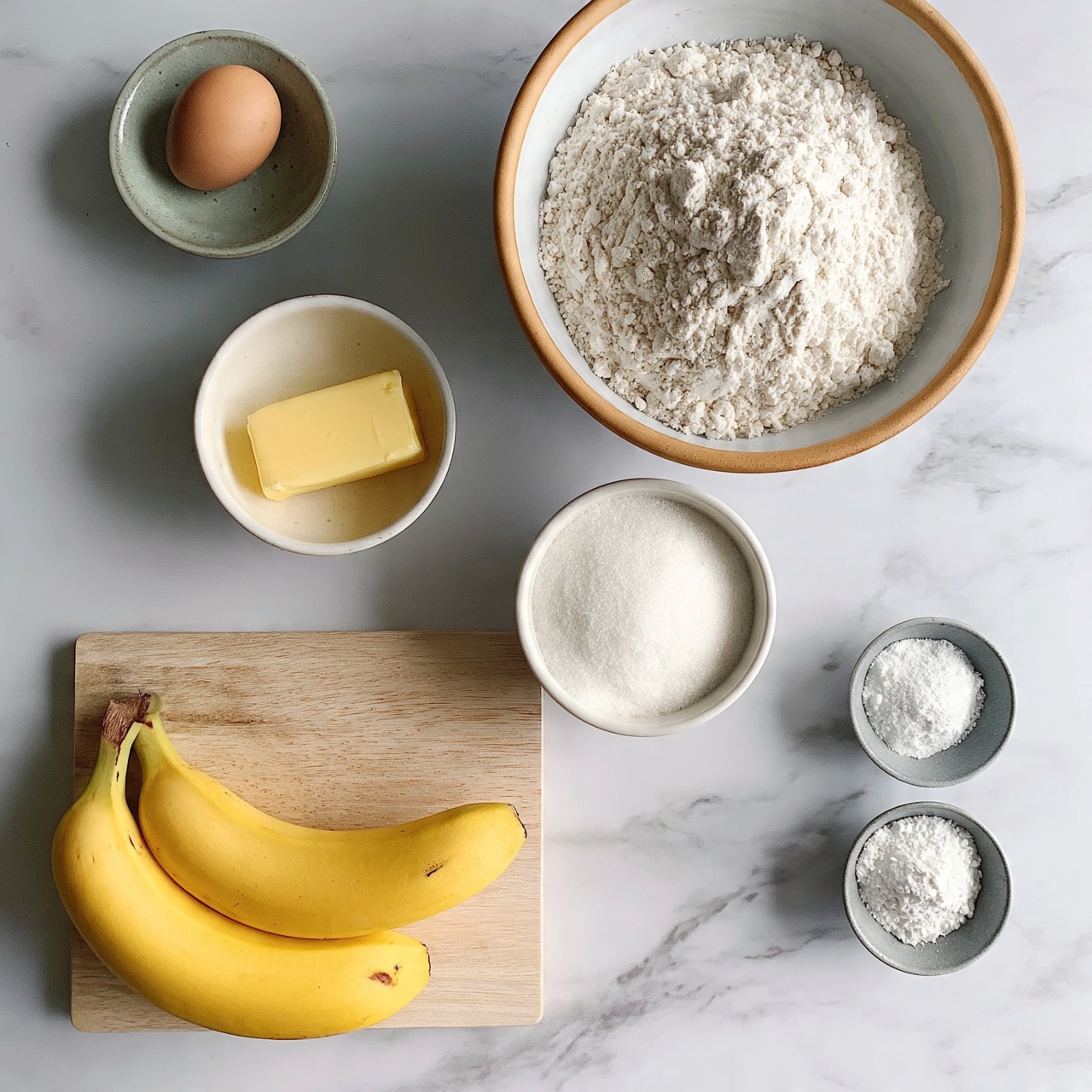 square image The image shows ingredients laid out on a white marbled surface, including two yellow bananas with small brown marks placed on a light wooden cutting board at the bottom left. Above the bananas, there is a small white bowl with a yellow stick of butter. To the top left there is a small greenish-gray bowl with a single brown egg inside. On the right side, there is a large white bowl with a tan rim filled with white flour. Below it, there is a smaller white bowl with sugar. To the right of that, two small gray bowls hold white powders. photo taken with an iphone --ar 4:5 --v 7