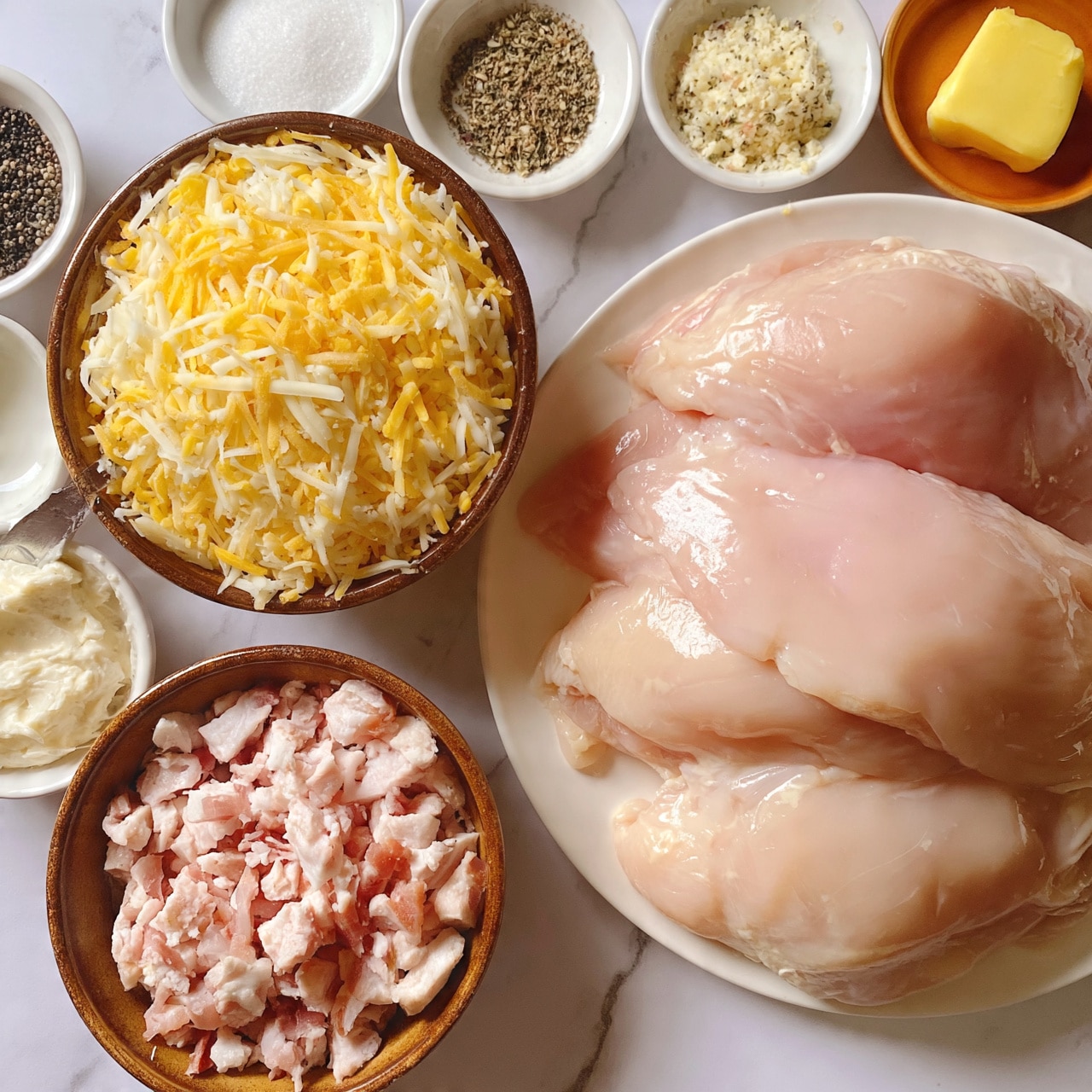 square imag  The image shows a flat lay of cooking ingredients on a white marbled surface. On the right, there is a white plate piled with four large raw chicken fillets, pale pink with glossy texture. Next to it, on the left, a brown bowl holds a mix of shredded yellow and white cheese. Below the chicken fillets, a brown bowl contains small chunks of pale pink bacon with white fat. Surrounding these bowls are smaller white dishes filled with white salt, black pepper, a mix of dry herbs and spices, soft white spread with a knife resting on the bowl's edge, and a pat of yellow butter on an orange dish. Everything is neatly arranged and clearly visible, photo taken with an iphone --ar 4:5 --v 7