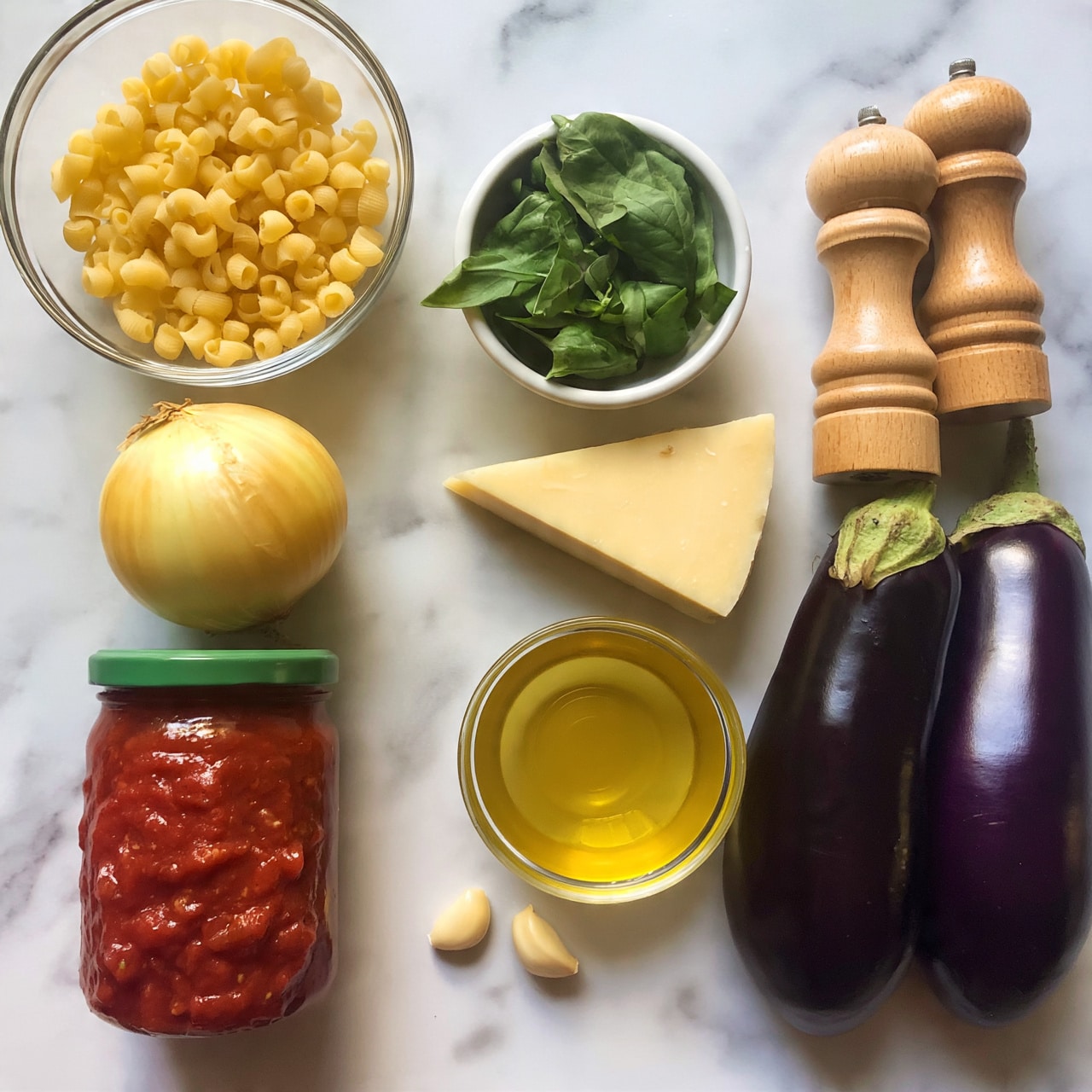 Ziti alla Norma (Eggplant and Tomato Pasta) Recipe 4 square image The image shows an overhead view of cooking ingredients arranged neatly on a white marbled surface. At the top left, there is a clear glass bowl filled with small yellow pasta pieces. Below that is a whole yellow onion and a jar of red tomato sauce with a green lid. Slightly above and to the right of the onion and sauce, a small white bowl holds fresh green basil leaves. Next to the basil bowl is a wedge of pale yellow cheese. To the right of the cheese is a small glass bowl of light yellow olive oil. Near the bottom center are two small garlic cloves. On the right side of the image, two dark purple eggplants lie next to two wooden pepper mills and salt grinders. The arrangement is clean and simple, all set on the smooth white marbled surface photo taken with an iphone --ar 4:5 --v 7