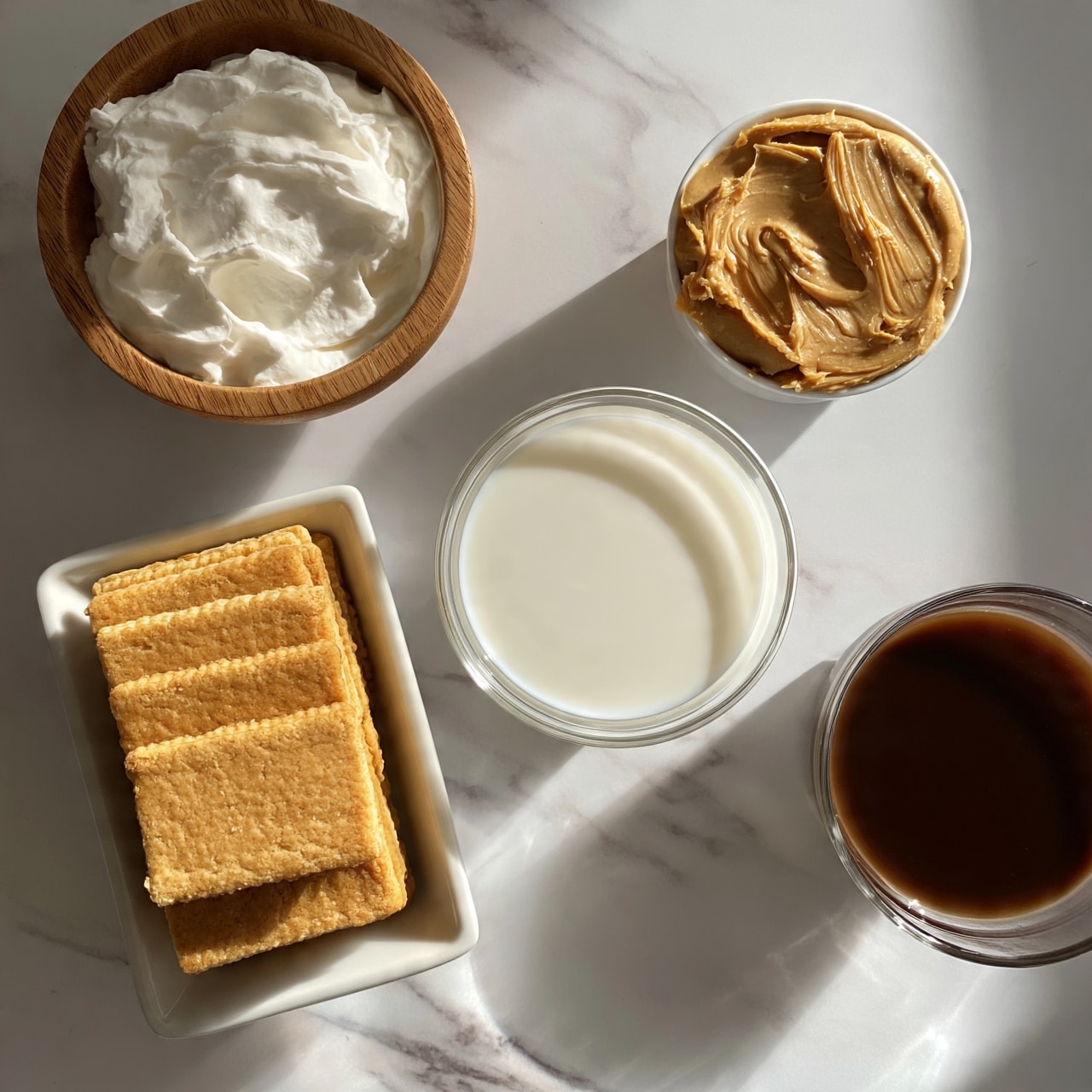square image The image shows five small white containers placed on a white marbled surface. On the top left, there is a wooden bowl filled with a thick white creamy substance, likely whipped cream. Below it, slightly to the right, is a white rectangular dish holding a neat stack of golden brown rectangular biscuits. In the center, a clear round bowl contains a milky white liquid, probably milk. Top right has a small white bowl filled with peanut butter, showing smooth, creamy texture with swirled ridges on the surface. Bottom right is another clear round bowl holding a dark brown liquid, likely coffee or a similar drink. photo taken with an iphone --ar 4:5 --v 7