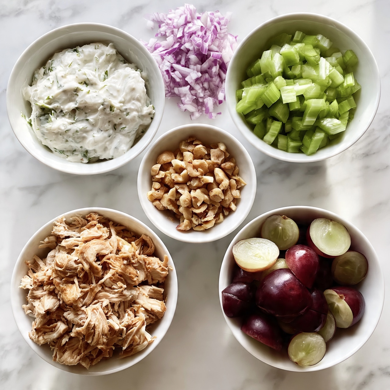 square image This image shows six white bowls on a white marbled surface. In the bottom left bowl is shredded light brown chicken. To the bottom right is a bowl filled with halved dark red grapes with pale green insides. Above that is a small white bowl with chopped light brown nuts. In the middle is a small white bowl with finely chopped red onions. On the top right is a bowl filled with chopped green celery. On the top left is a bowl with thick white sauce mixed with green herbs. photo taken with an iphone --ar 4:5 --v 7