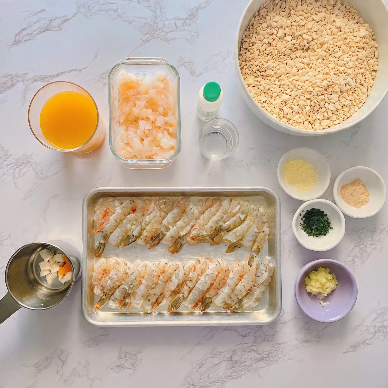 square image The image shows a white marbled background with several items arranged neatly. In the center, there is a silver tray filled with raw shrimp placed in two rows. On the left side of the tray, a metal measuring cup holds small white and orange pieces. Above the tray, there is a glass container with peeled shrimp. To the left of it, there is a glass filled with orange liquid. To the right of the glass container, a small white bottle with a green cap stands alongside a small clear glass of clear liquid. On the upper right corner, a large white bowl filled with light beige crushed crackers is visible. Below it, there are three small white bowls with different contents: one with pale yellow crumbs, another with chopped green herbs, and the last one with a light brown powder. A small purple bowl holds minced light yellow garlic. Everything is clearly placed on the white marbled surface photo taken with an iphone --ar 4:5 --v 7