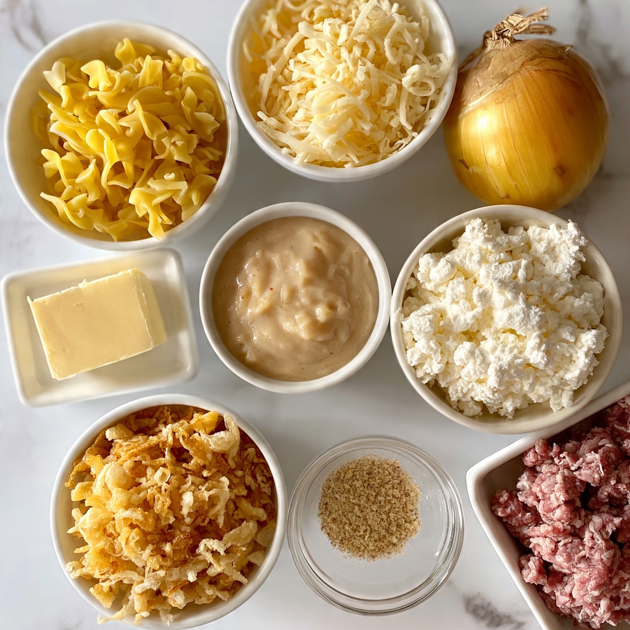 square image The image shows several white bowls and dishes arranged on a white marbled surface, each filled with different ingredients. One bowl contains yellow dried egg noodles with a twisted shape. Another holds shredded pale yellow cheese with a fine, soft texture. A small white dish has a rectangular block of pale yellow butter. There's a whole yellow-brown onion with a shiny outer skin. A small bowl contains light brown creamy sauce with a slightly lumpy texture. A bowl holds crumbled white soft cheese with a crumbly, airy texture. Another bowl is filled with crunchy, golden fried onions with an uneven texture. A small clear bowl contains light brown dried seasoning or spices. Finally, a white dish holds a portion of raw ground meat in a coarse, chunky texture. Photo taken with an iphone --ar 4:5 --v 7