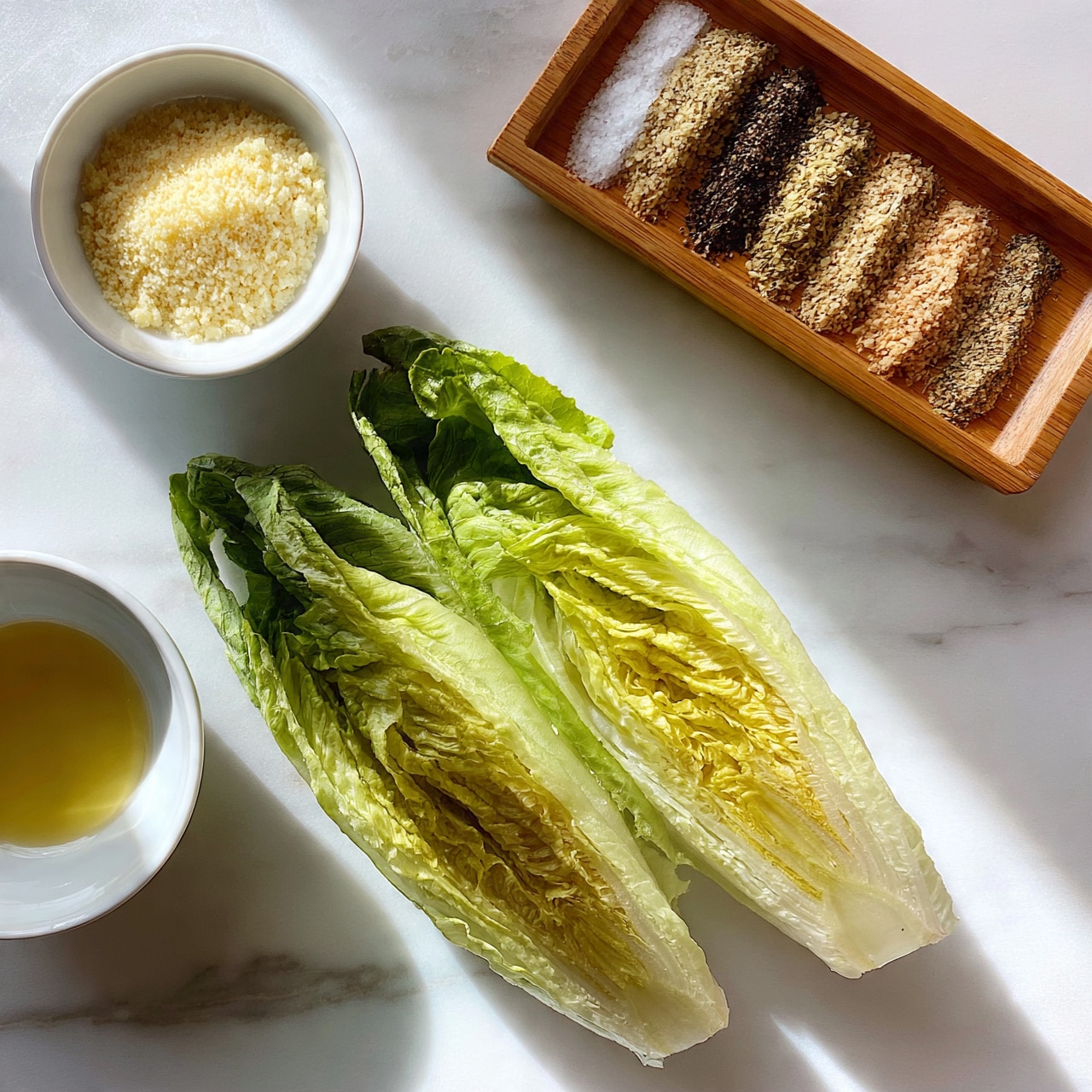 square image The image shows two halves of fresh green romaine lettuce with visible leafy layers and a crisp texture placed diagonally on a white marbled surface. To the left, there is a small white bowl filled with light golden oil, and above it a small white bowl containing a coarse, pale lemon-yellow powder. At the top right, a wooden rectangular tray holds six small piles of different spices arranged in horizontal rows, including salt, black pepper, and other mixed herbs in light brown and beige shades. The layout is simple and clean with soft natural light casting gentle shadows. photo taken with an iphone --ar 4:5 --v 7