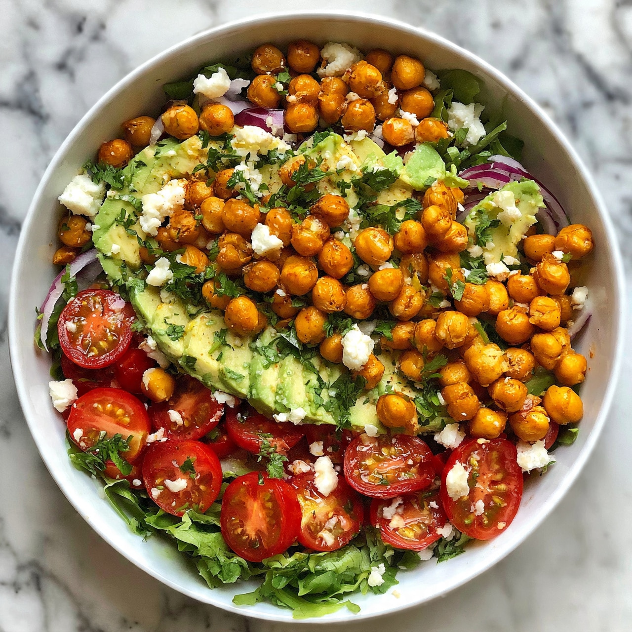 square image A white bowl filled with a colorful salad on a white marbled surface, featuring multiple layers: at the base there are fresh green leafy vegetables, topped with bright red cherry tomato halves, creamy slices of light green avocado, crunchy golden-brown roasted chickpeas scattered evenly, garnished with small chunks of white cheese and fresh green parsley, with thin slices of purple onion adding a touch of contrast, photo taken with an iphone --ar 4:5 --v 7