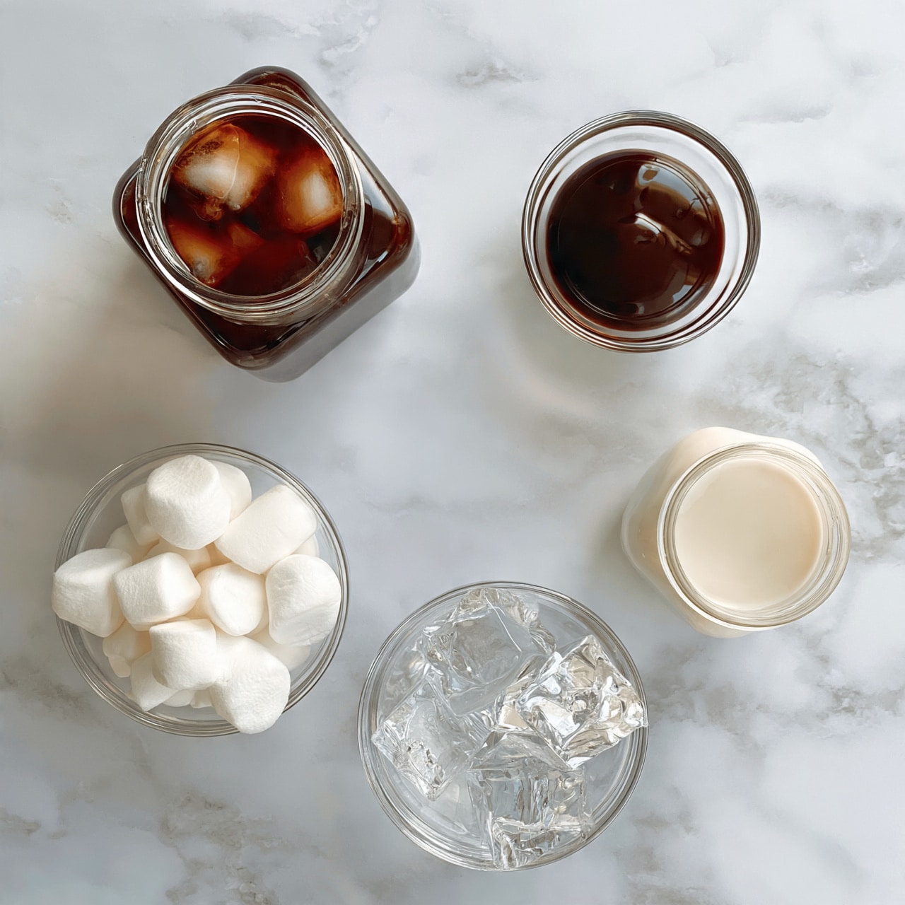 square image The image shows a white marbled background with five items arranged on it. At the top left is a square glass jar filled with dark brown liquid and some ice cubes inside. To the right is a small clear glass bowl containing a smooth, shiny dark brown sauce. Below the jar, there is another clear glass bowl filled with white marshmallows, stacked with soft, round tops. On the right side near the marshmallows is a small glass jar filled with a light cream-colored liquid. At the bottom center is a clear glass bowl holding several large, clear ice cubes with sharp edges. The lighting highlights the textures and colors clearly. Photo taken with an iphone --ar 4:5 --v 7