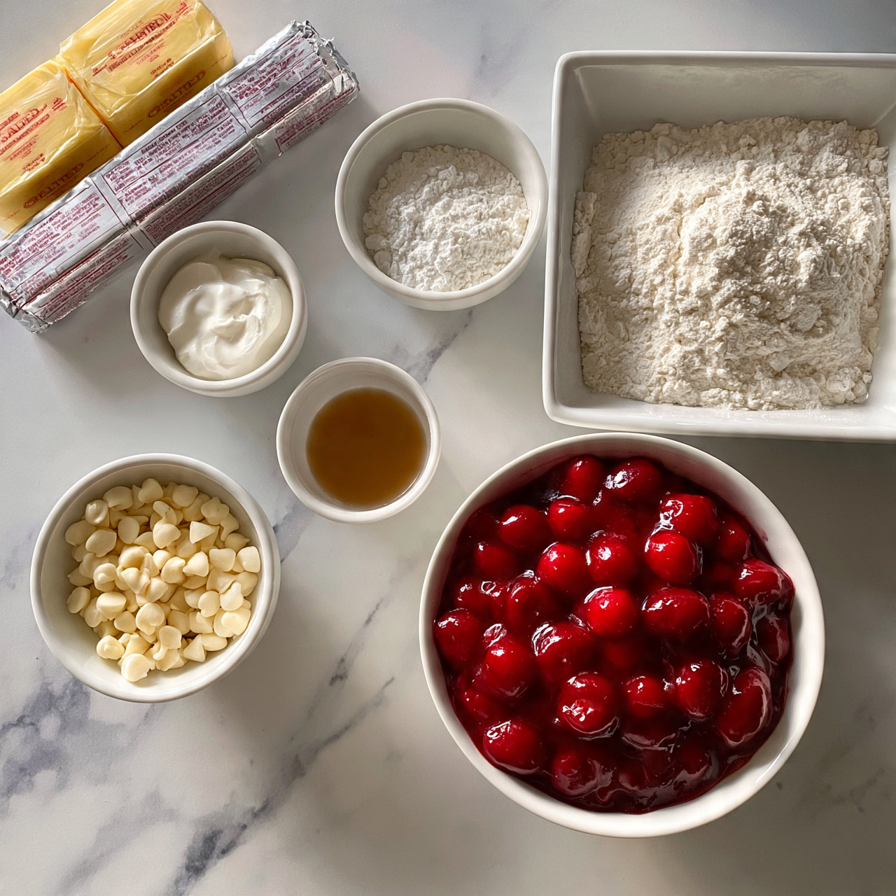Strawberry Cream Cheese Dump Cake Recipe 4 square image The image shows multiple white bowls and a white square dish arranged on a white marbled surface, each filled with different baking ingredients. In the center back, there is a small round bowl filled with white powder, likely flour or powdered sugar. To the right, a large white square dish contains more white powder, probably flour. Below that, a large white bowl is filled with bright red cherry pie filling, glossy with whole cherries visible. To the left of the cherry filling, a small white bowl holds many small white chips, resembling baking chips. Above it sits a tiny white bowl with a light brown liquid, likely vanilla extract. Next to it, there is a small round bowl filled with a white creamy substance, possibly sour cream. At the top left corner, two sticks of yellow salted butter wrapped in paper lie next to a rectangular silver wrapped block, likely cream cheese, with text visible on the wrappers. The overall setting is clean and organized, viewed from above. Photo taken with an iphone --ar 4:5 --v 7