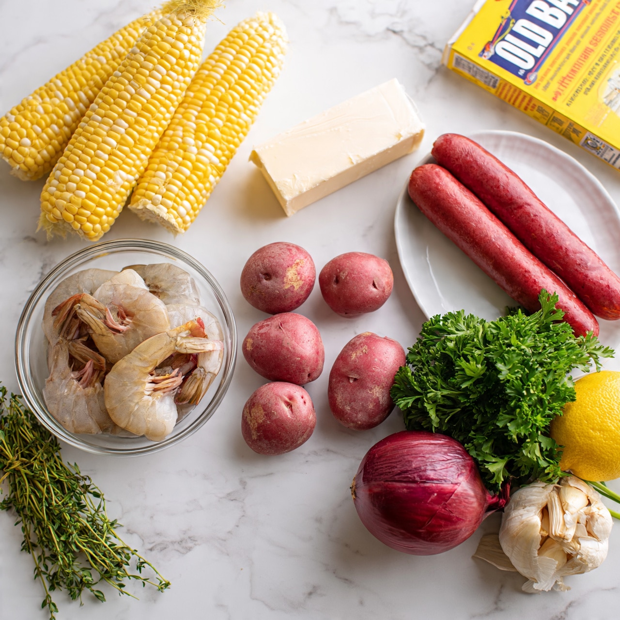 square image The image shows raw ingredients arranged on a white marbled surface. There are three fresh yellow ears of corn positioned at the top left. Below the corn, a clear glass bowl holds several raw shrimp with shells on. To the right of the shrimp, there are five small red potatoes scattered in a loose cluster. Above the potatoes, a white block of butter lies horizontally. Adjacent to the potatoes on the right, two long, red sausages rest side by side on a white plate. Next to the sausages is a small bunch of fresh green parsley. A red onion sits below the parsley and to the right of the potatoes. Near the onion and to the far right is a whole lemon and a bulb of garlic. Toward the top right, a box of Old Bay seasoning is visible. A small bunch of fresh thyme is placed on the far left side. Photo taken with an iphone --ar 4:5 --v 7