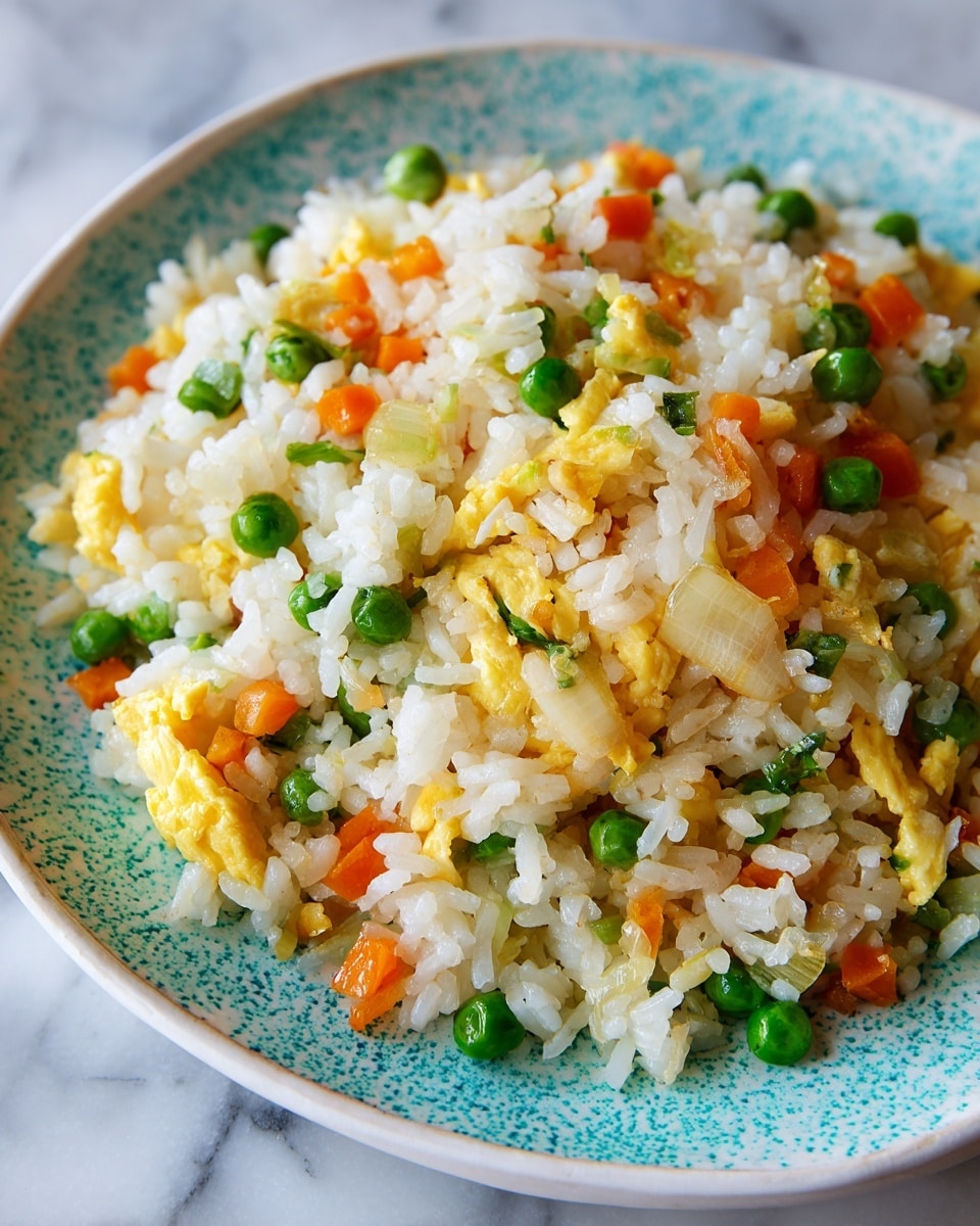 square image A close-up view of fried rice served on a white plate with a speckled turquoise pattern, filled with small white rice grains mixed with bright green peas, light yellow scrambled eggs, finely chopped orange carrots, and small pieces of translucent sautéed onions. The rice looks fluffy with a slight shine, and the vegetables are evenly spread throughout the dish, creating a colorful and textured look. The background shows a white marbled surface. photo taken with an iphone --ar 4:5 --v 7