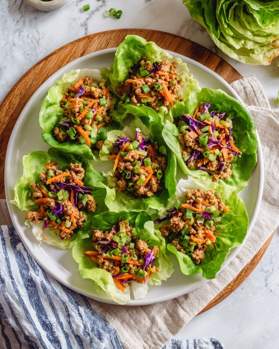 A white round plate holds seven bright green lettuce cups, each filled with a mixture of finely chopped cooked meat and vegetables. The filling is a mix of light brown minced meat with hints of orange carrot shreds and small bits of purple cabbage, topped with chopped green onions. The lettuce leaves are fresh and crisp, forming natural cups that cradle the filling. The plate rests on a wooden round board with a beige cloth and a blue and white striped cloth nearby on a white marbled surface. In the top right corner, part of a green lettuce head and a woman's hand holding it are visible. Photo taken with an iphone --ar 4:5 --v 7