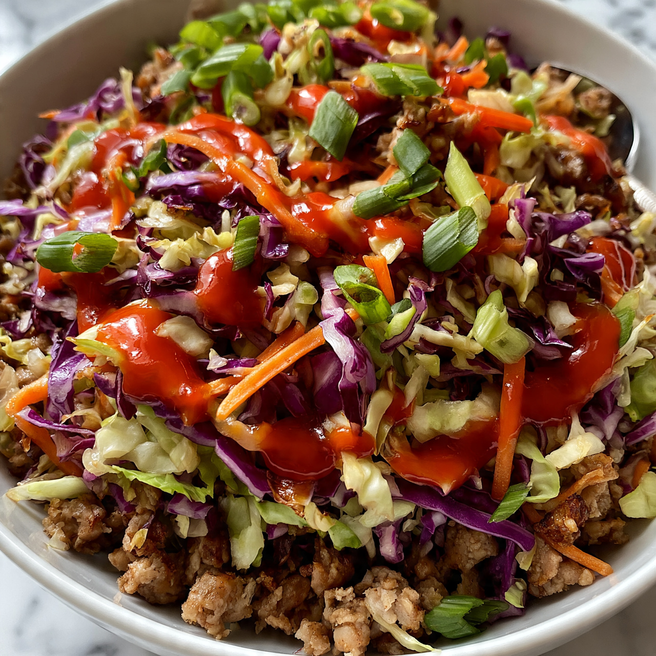 square image A close-up view of a white bowl filled with a colorful stir-fry dish, featuring three main layers: a base of browned small meat pieces, mixed with a layer of shredded purple and light green cabbage, thin orange carrot sticks, and sliced green onions scattered on top. Bright red sauce is drizzled unevenly across the surface, adding a splash of color and shine over the mix of textures, from crunchy vegetables to tender meat bits. The bowl rests on a white marbled surface, with a spoon partially visible on the side. Photo taken with an iphone --ar 4:5 --v 7