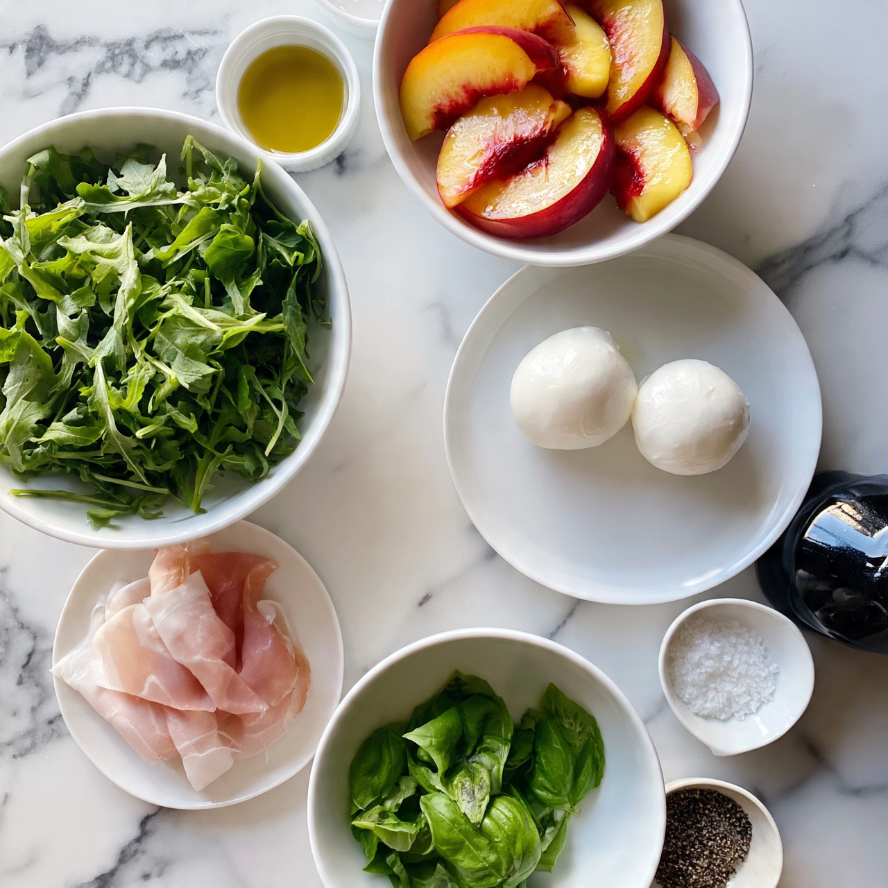 square image A top view of seven white bowls and plates arranged on a white marbled surface. One bowl at the top right holds sliced peaches with red skin and yellow flesh, showing a glossy texture. Below it, a white plate carries two white mozzarella balls with a smooth, shiny surface. To the left, a larger white bowl is filled with fresh green arugula leaves. Near the bottom left, a small white plate with light pink slices of prosciutto is placed. Below it, a small white bowl contains bright green basil leaves, showing some texture. Scattered around are small bowls with coarse salt, black pepper, and light yellow olive oil. There is also a bottle of dark balsamic glaze lying on its side near the mozzarella plate. The arrangement is clean and bright, with natural colors and textures standing out against the white marbled background. Photo taken with an iphone --ar 4:5 --v 7